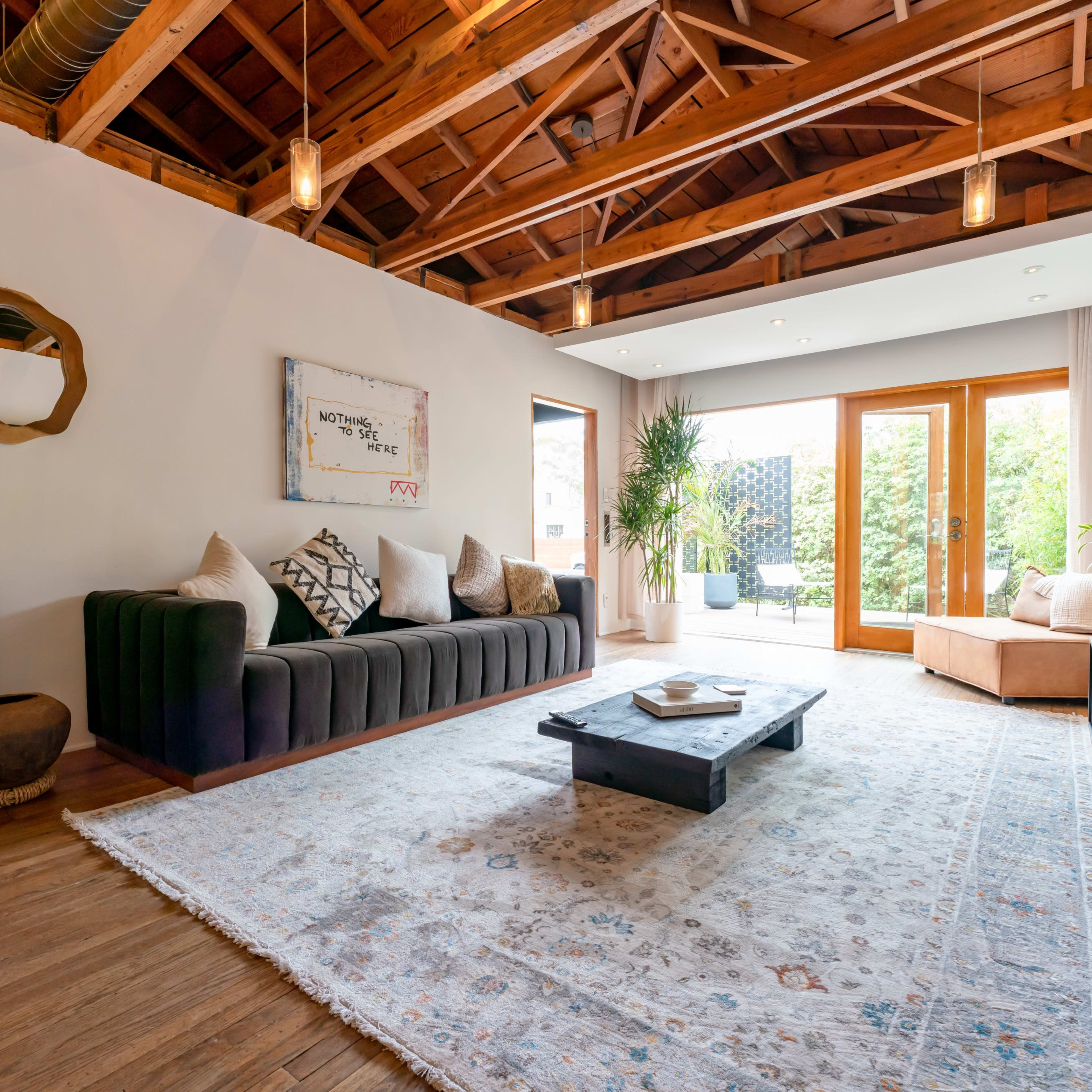A modern living room with a sectional couch, a coffee table, and large windows that open to a garden space.