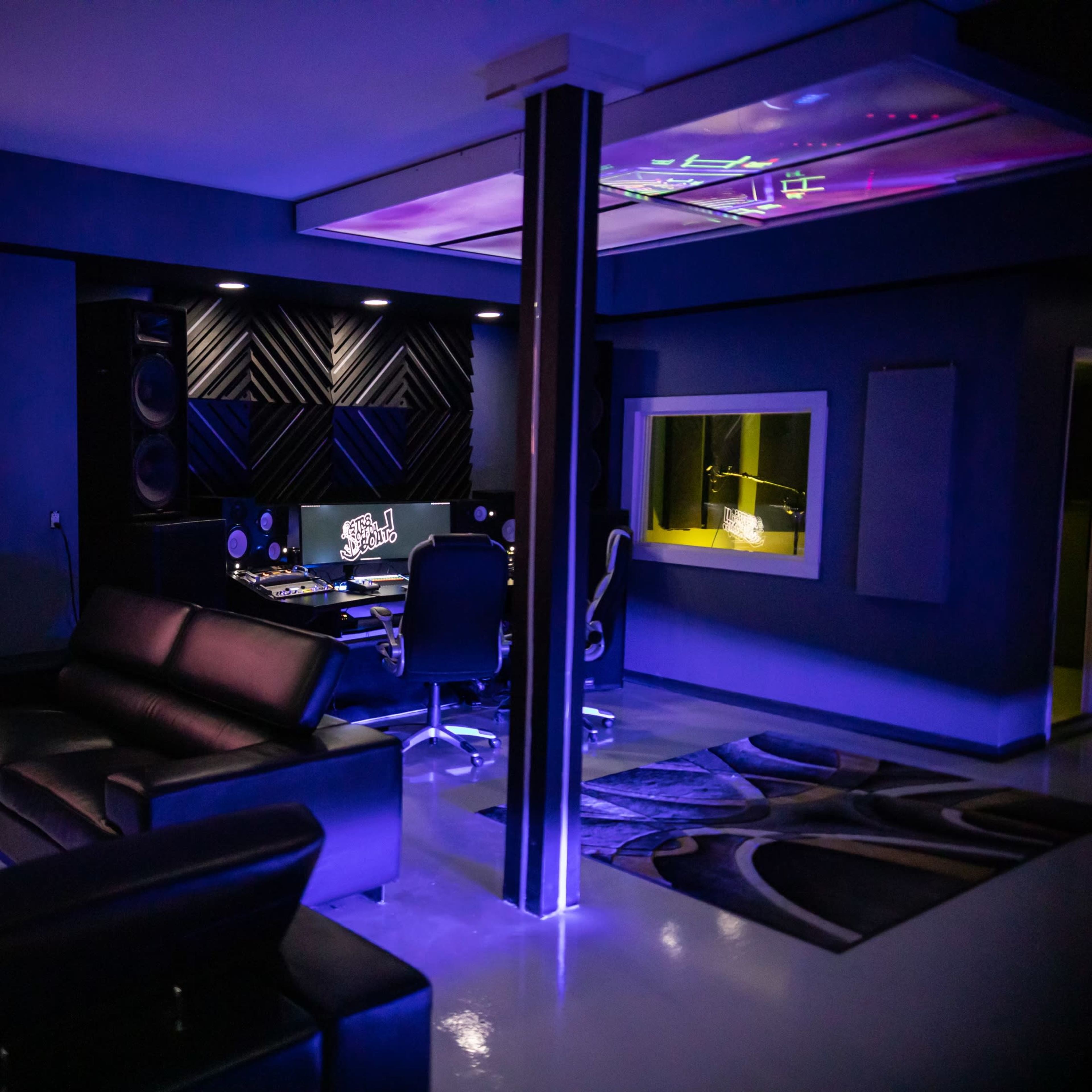 A modern music studio featuring a control room with a mixing console, a comfortable seating area, and ambient lighting.