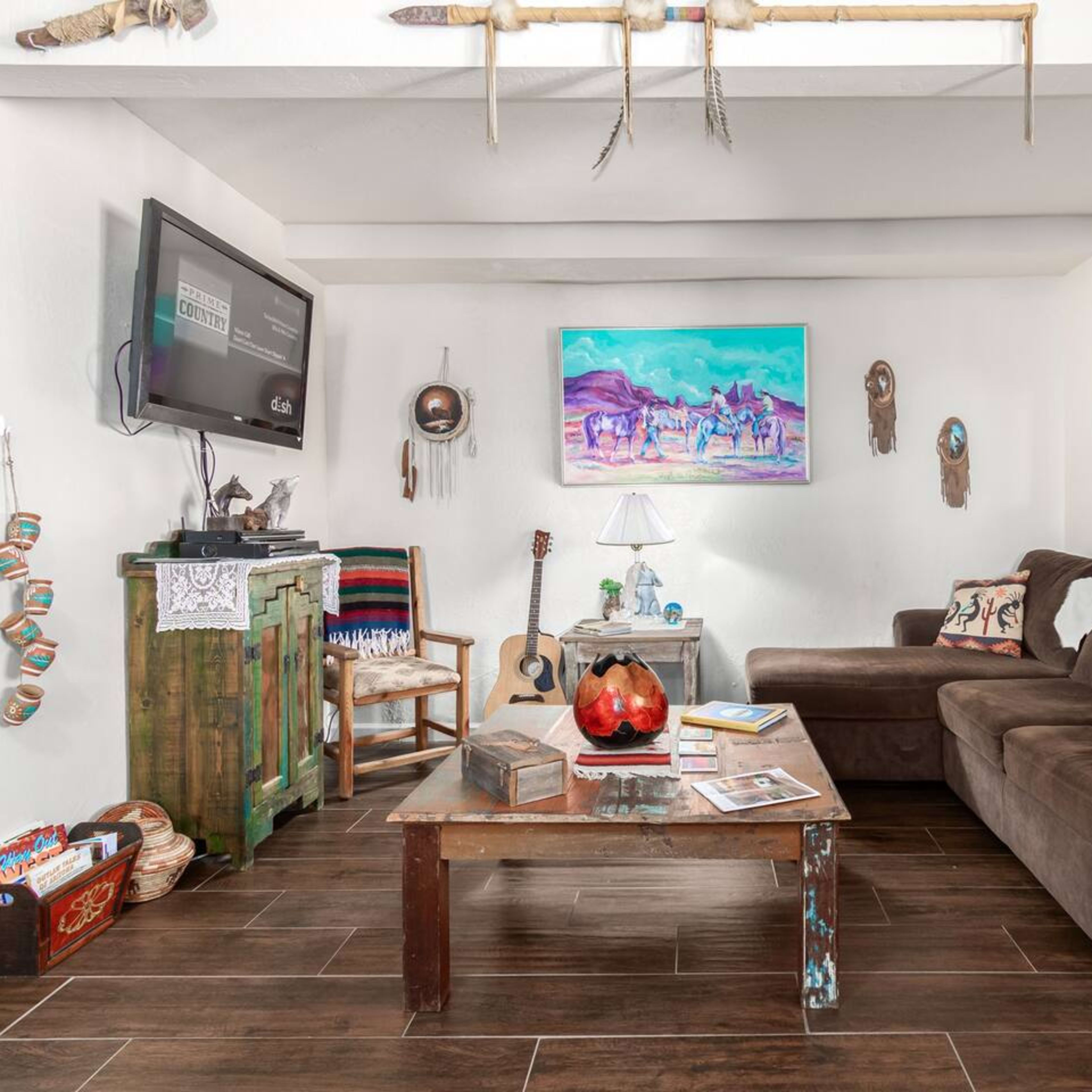 A living room with a brown couch, a wooden coffee table, a guitar, and various decorative items on the walls.