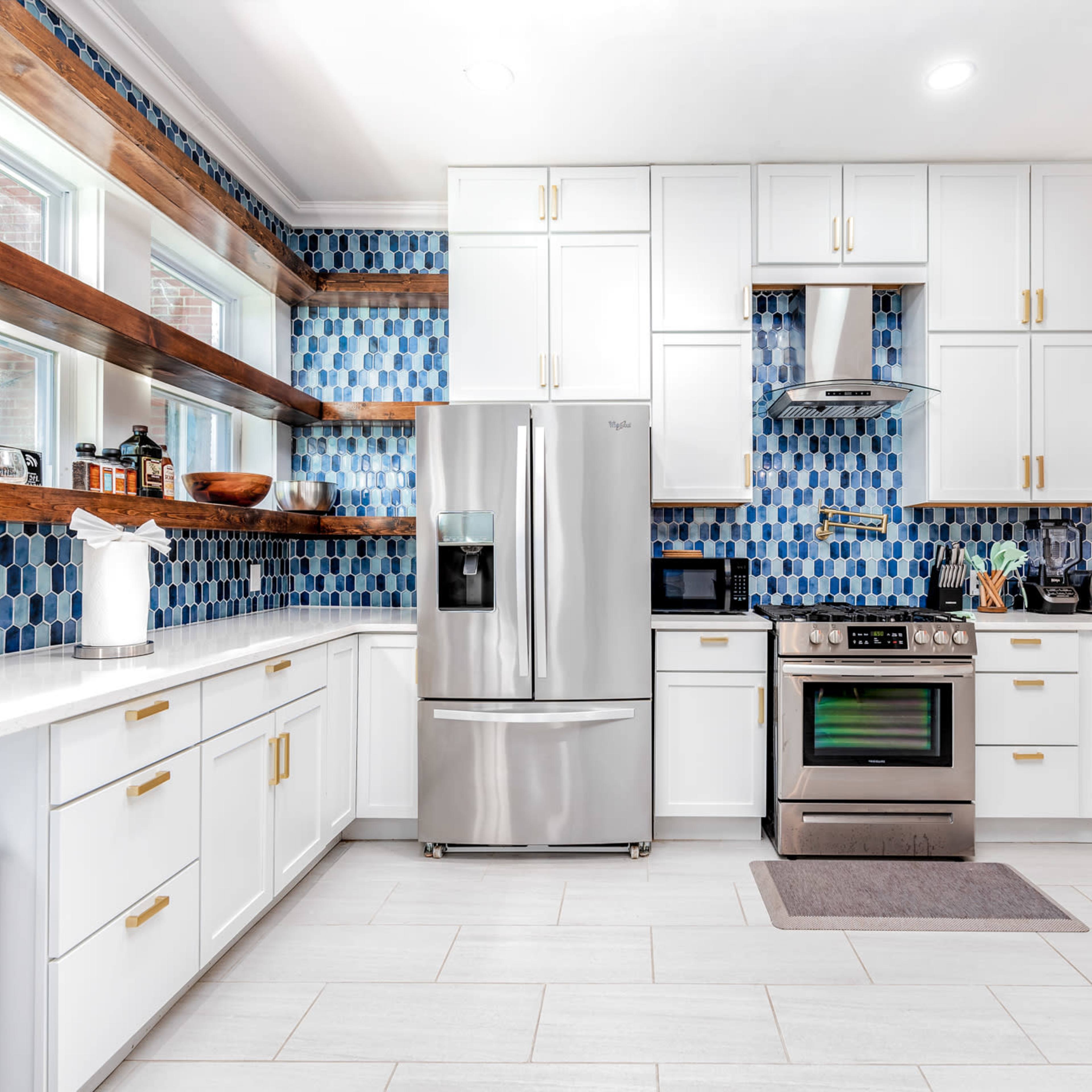 A modern kitchen features white cabinets, a stainless steel refrigerator, and a blue hexagonal tile backsplash.