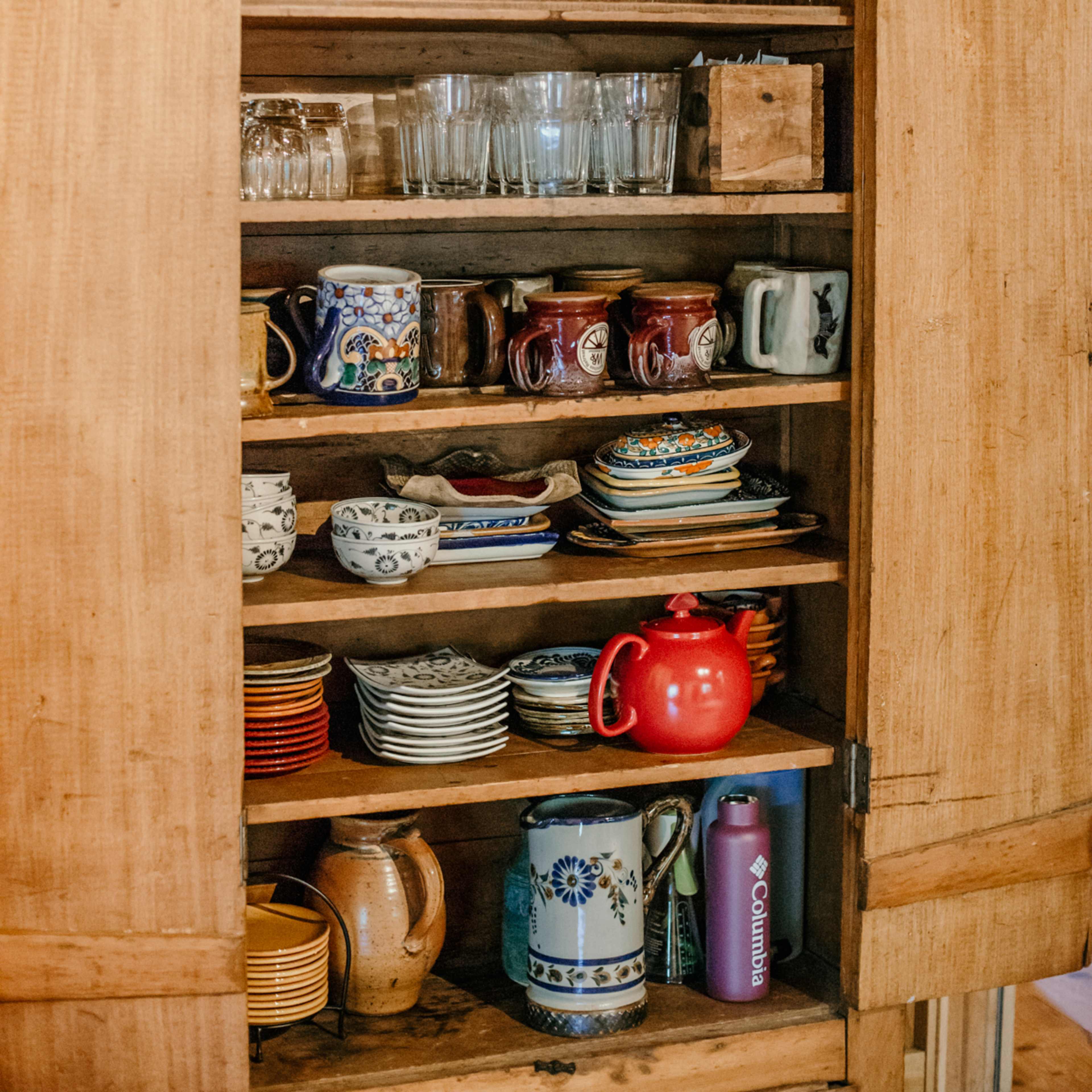 A wooden cupboard displays various types of glassware, mugs, and decorative dishes.