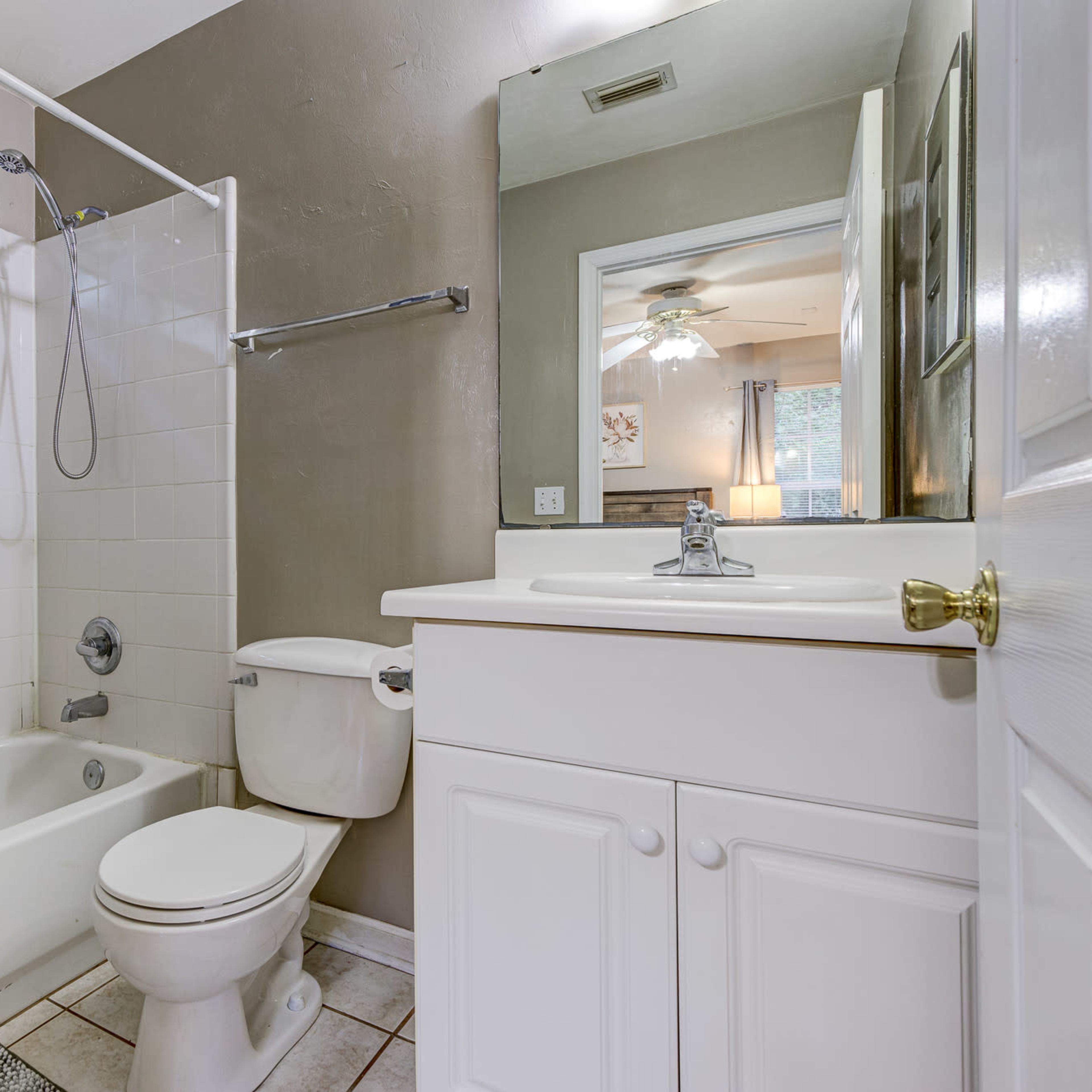 A bathroom with a bathtub and shower combination, a toilet, and a sink with a mirror reflecting a ceiling fan in the background.