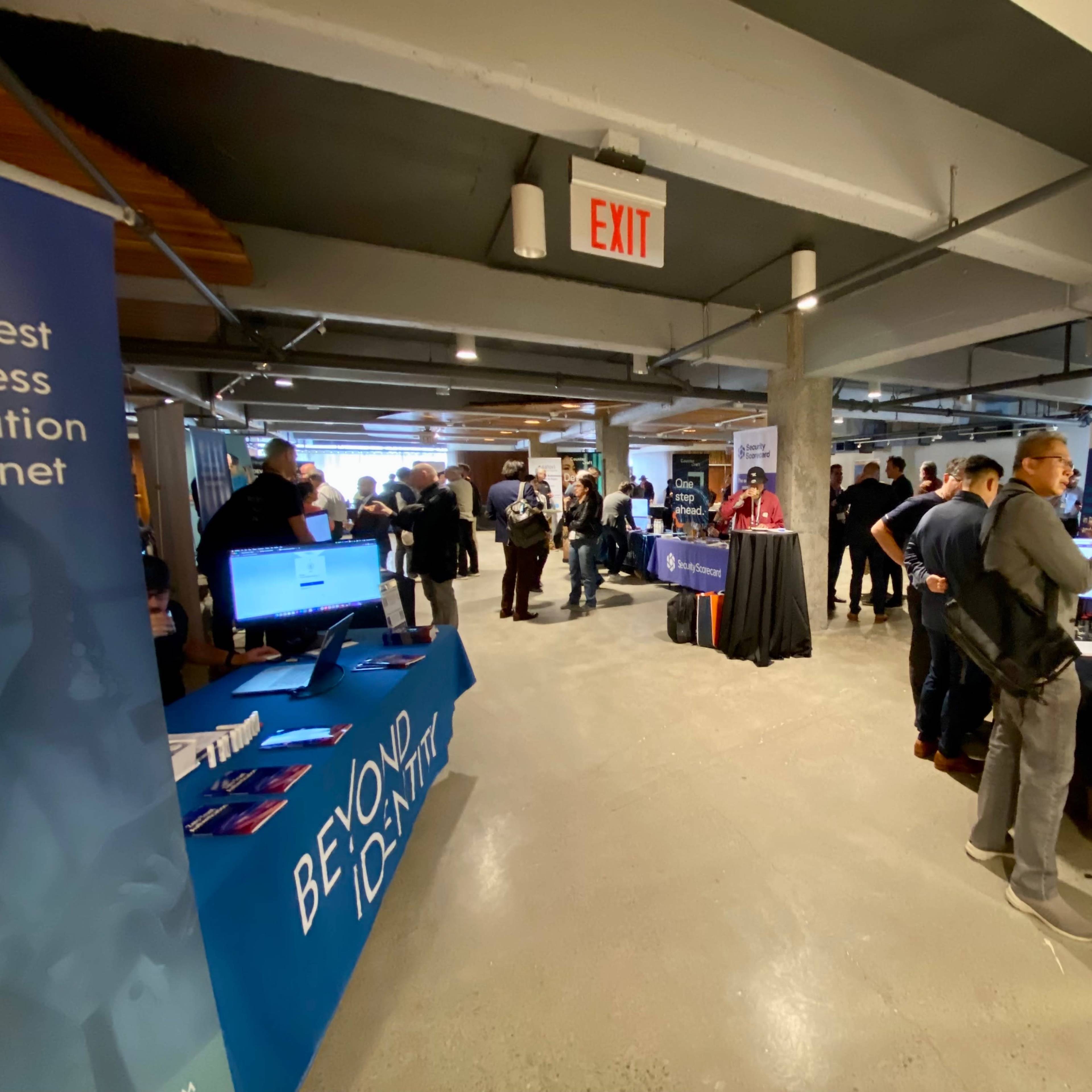 A conference hall is filled with attendees engaged in discussions at various display booths promoting technology and software solutions.