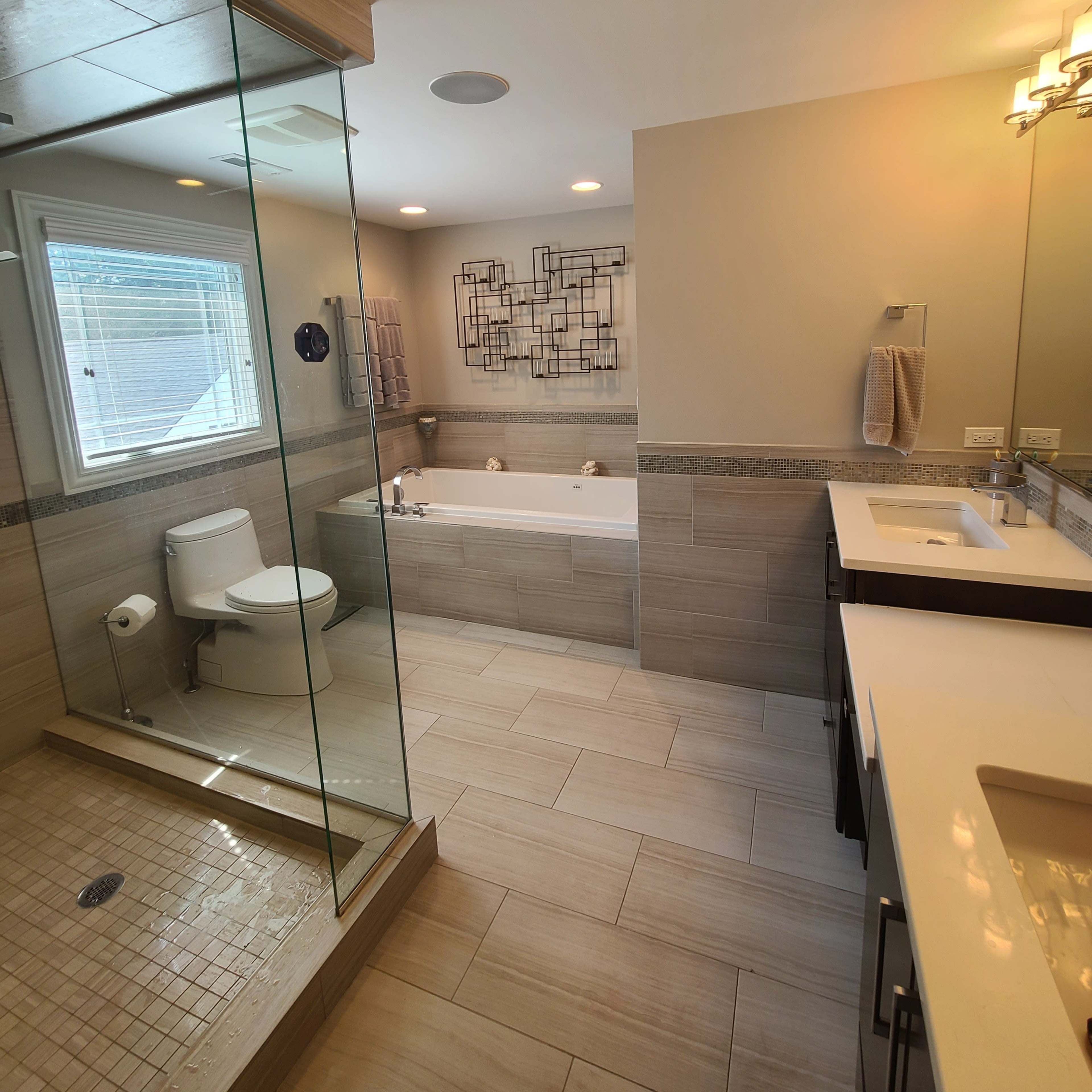 A modern bathroom featuring a glass shower enclosure, a bathtub, dual sinks with vanities, and neutral tile throughout.
