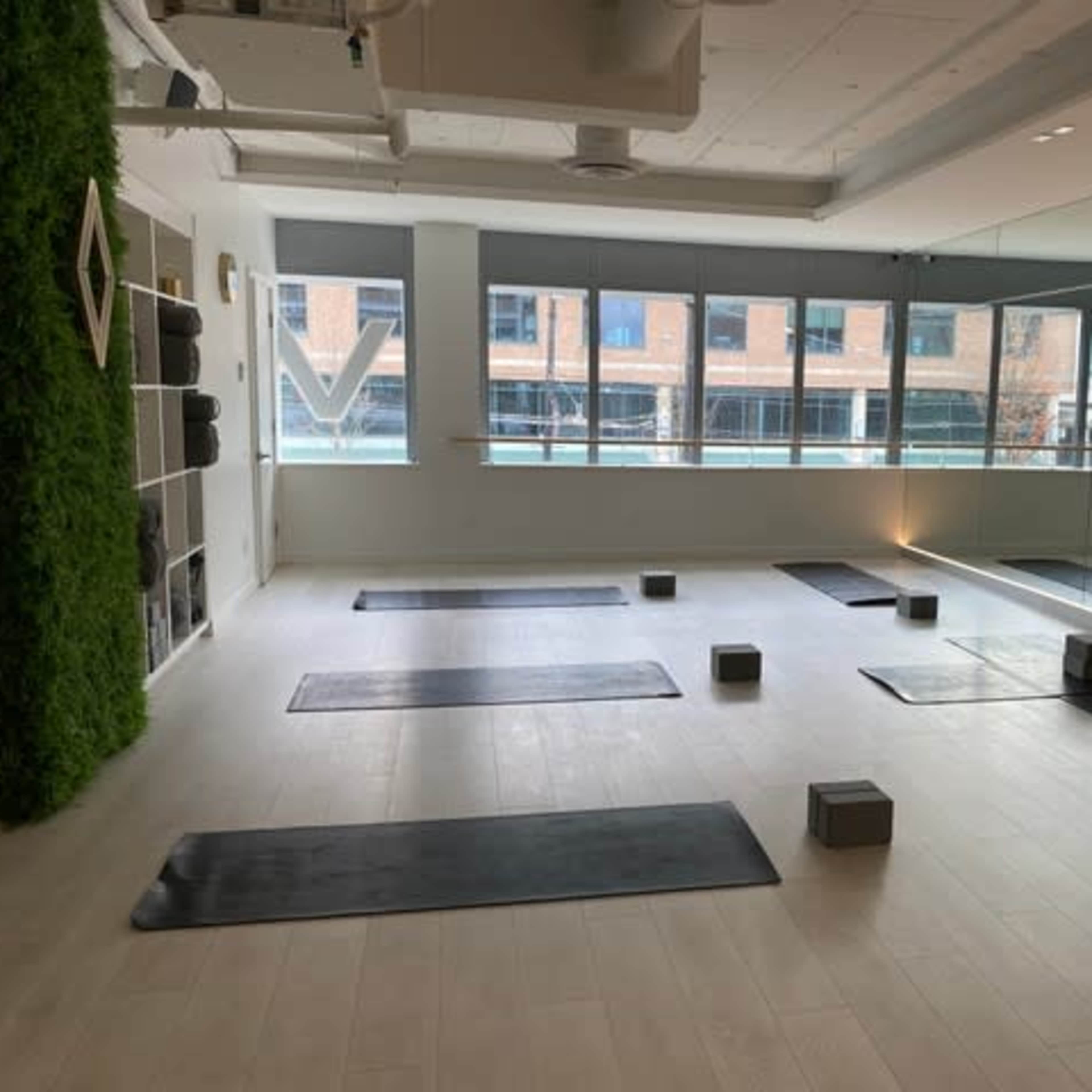 A spacious yoga studio with several yoga mats and blocks neatly arranged on the floor, along with large mirrors and windows providing natural light.