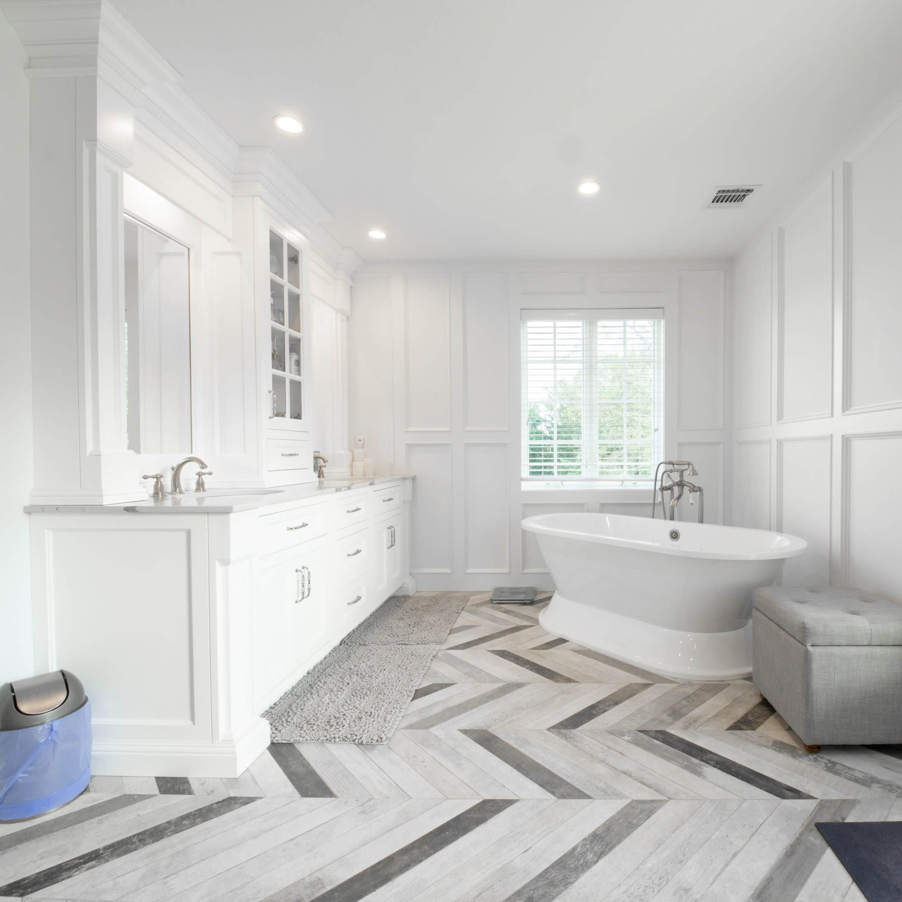 A modern bathroom features a freestanding bathtub, double vanity, and large windows allowing natural light.