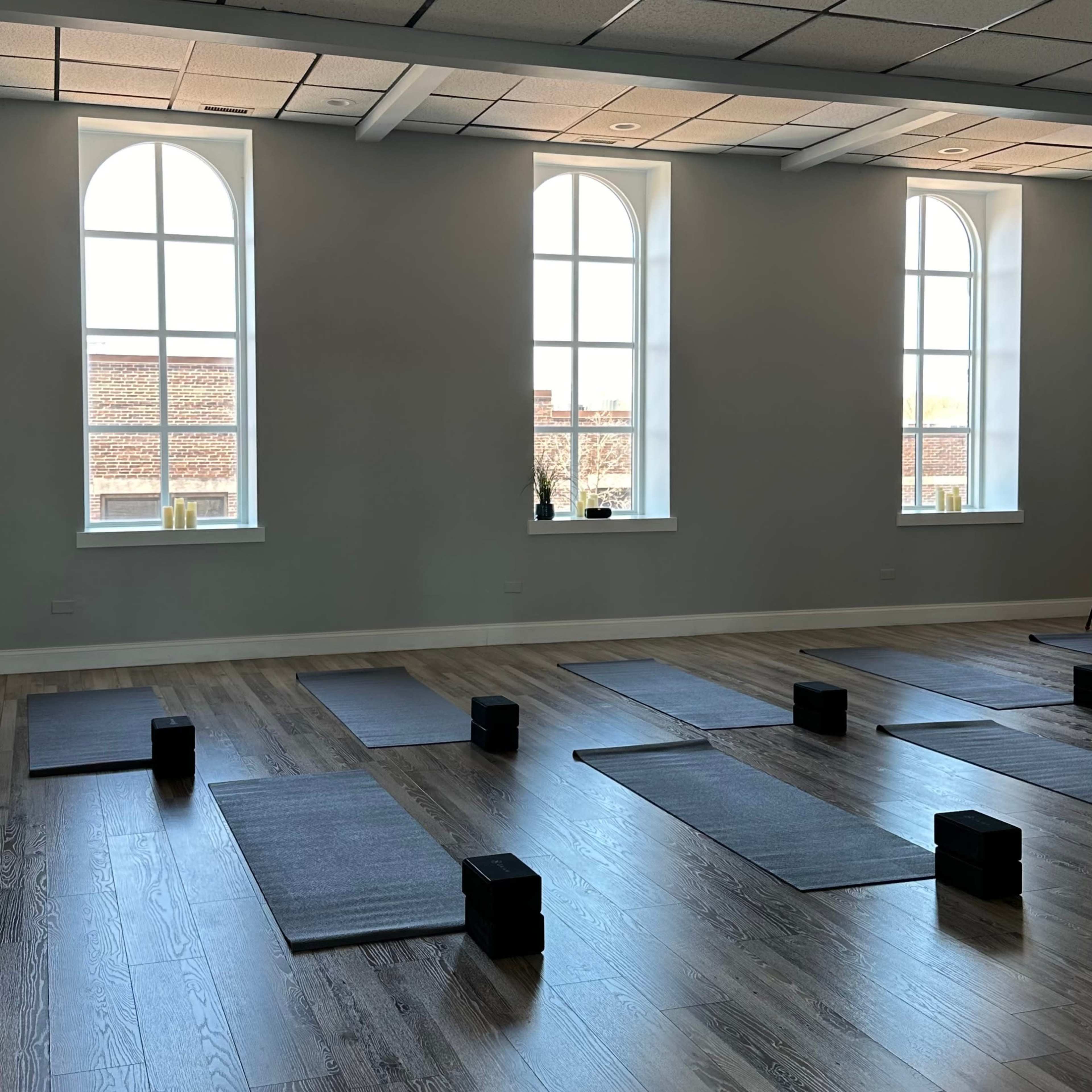A yoga studio with several mats arranged on the wooden floor beneath large, arched windows.