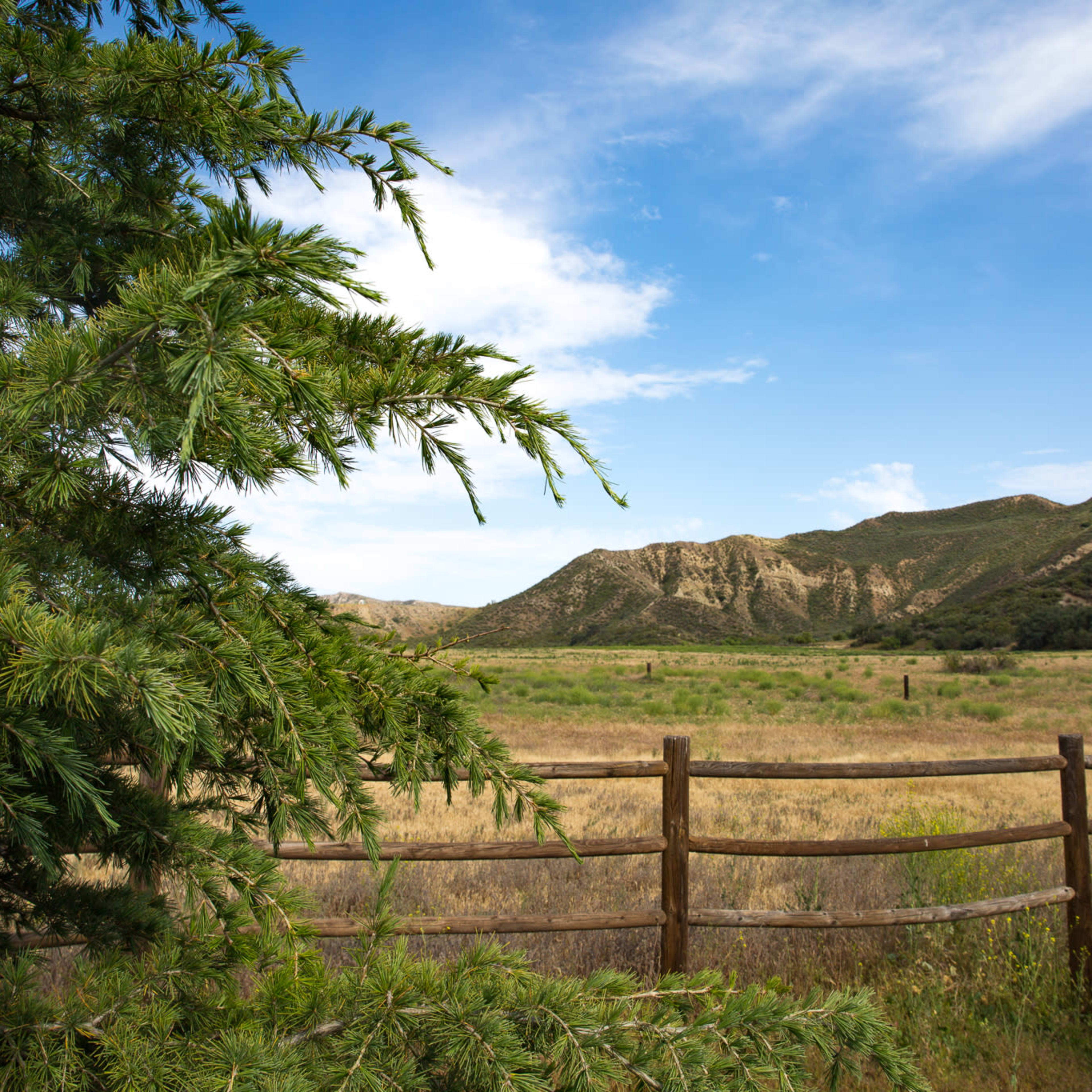A landscape with a wooden fence, a grassy field, and distant mountains under a partly cloudy sky.