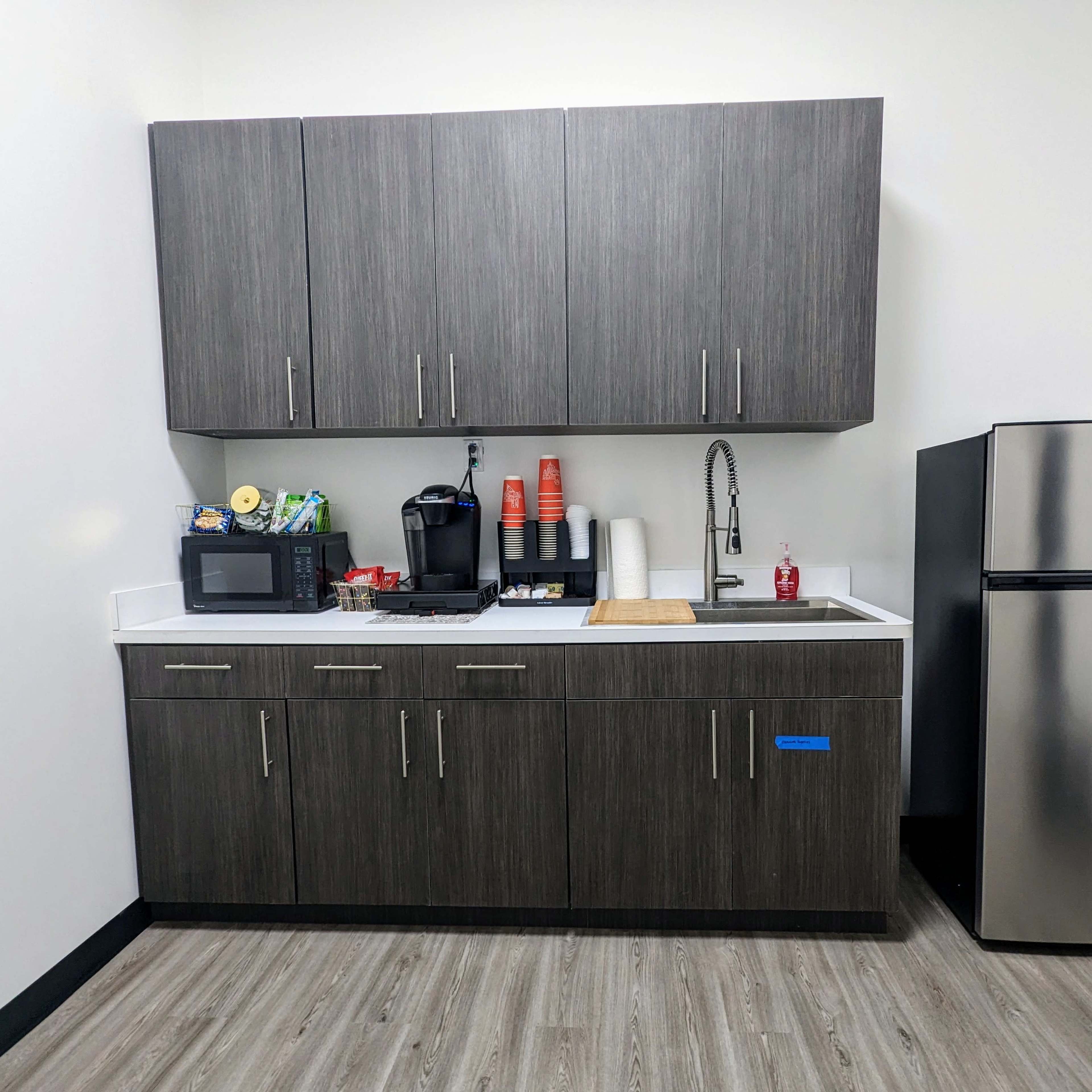 A modern kitchen corner with dark cabinetry, a microwave, a coffee maker, and a stainless steel refrigerator.