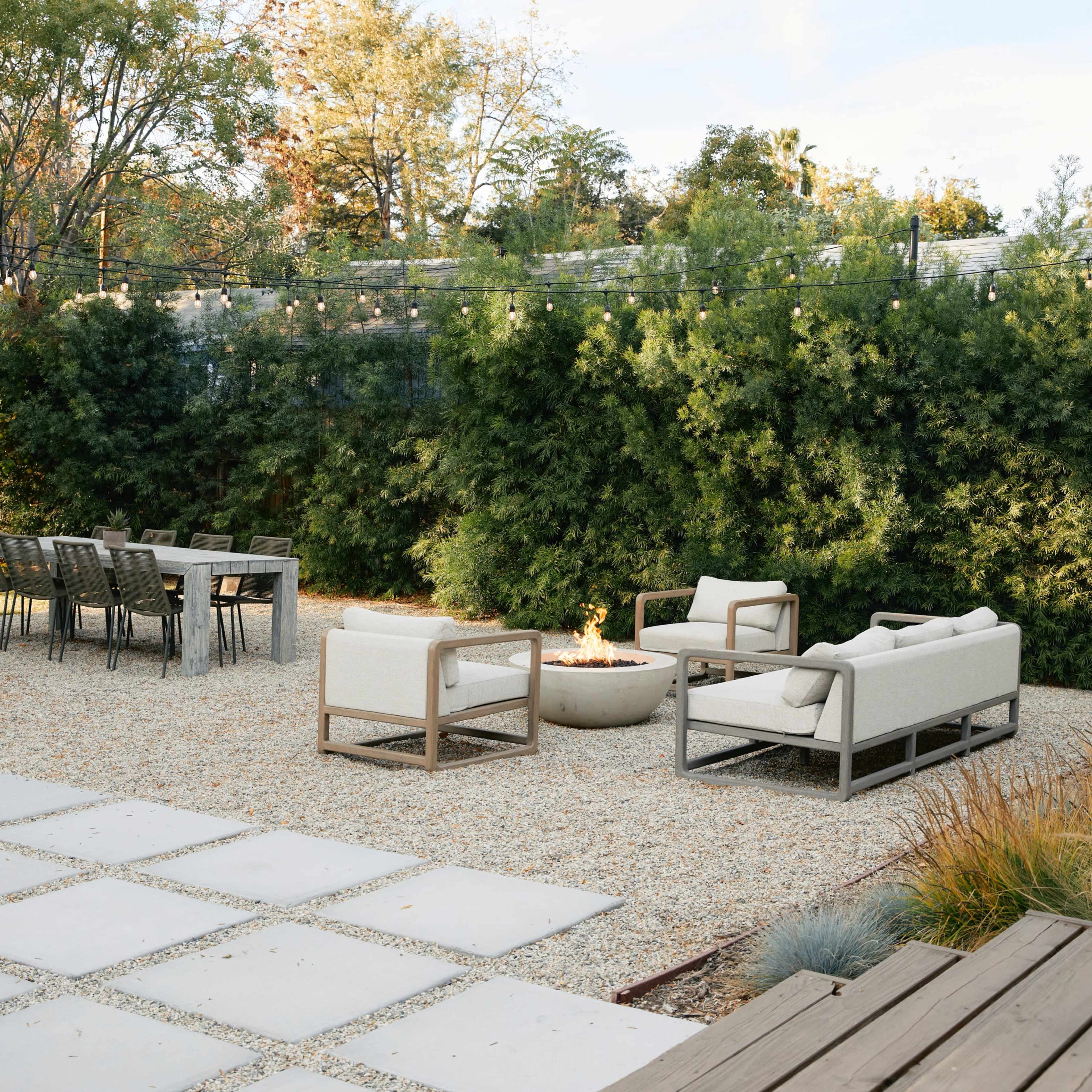 A landscaped outdoor space featuring a gravel area with a seating arrangement around a fire pit and a dining table nearby.