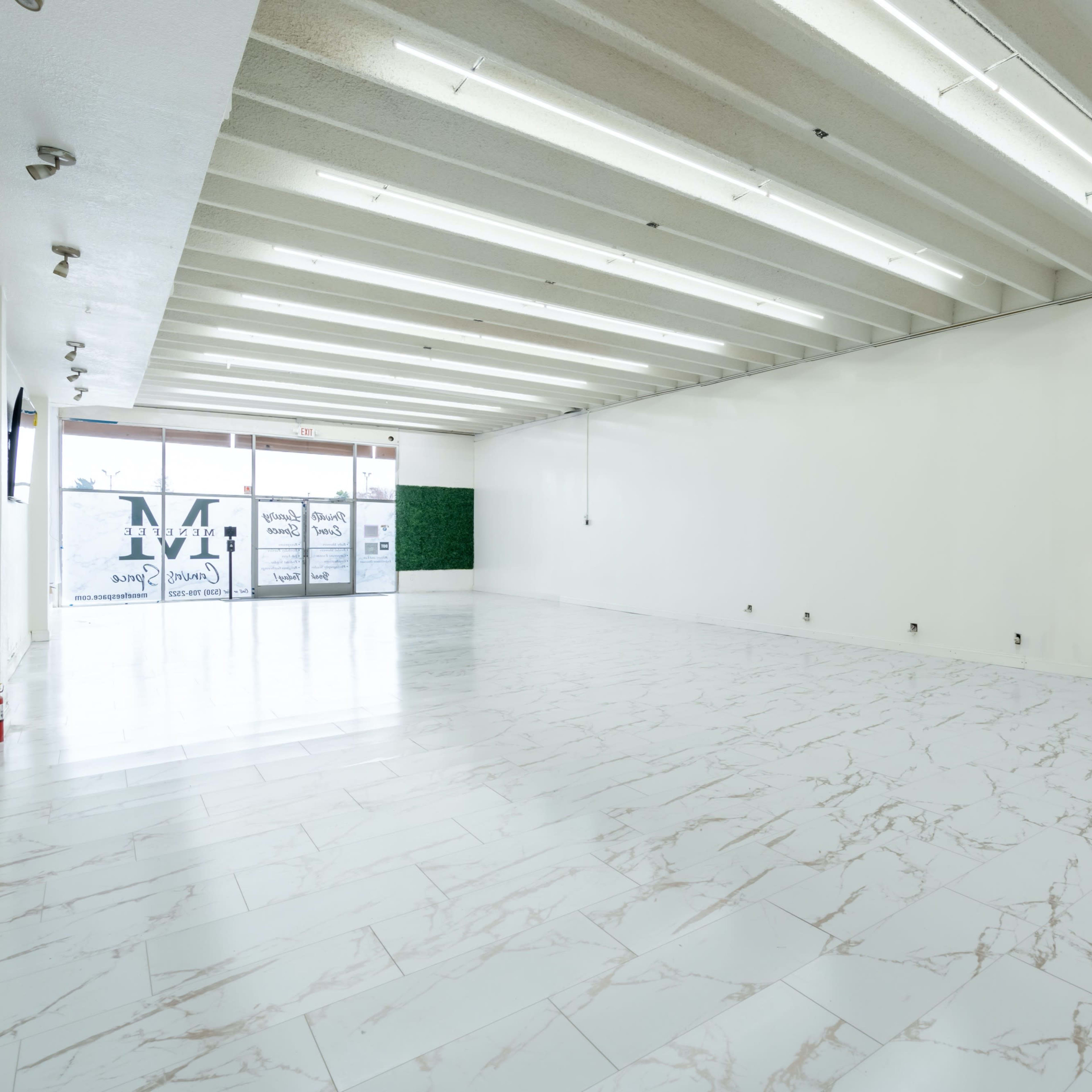 A spacious, empty interior with white walls, a marble-patterned floor, and large windows at the front.