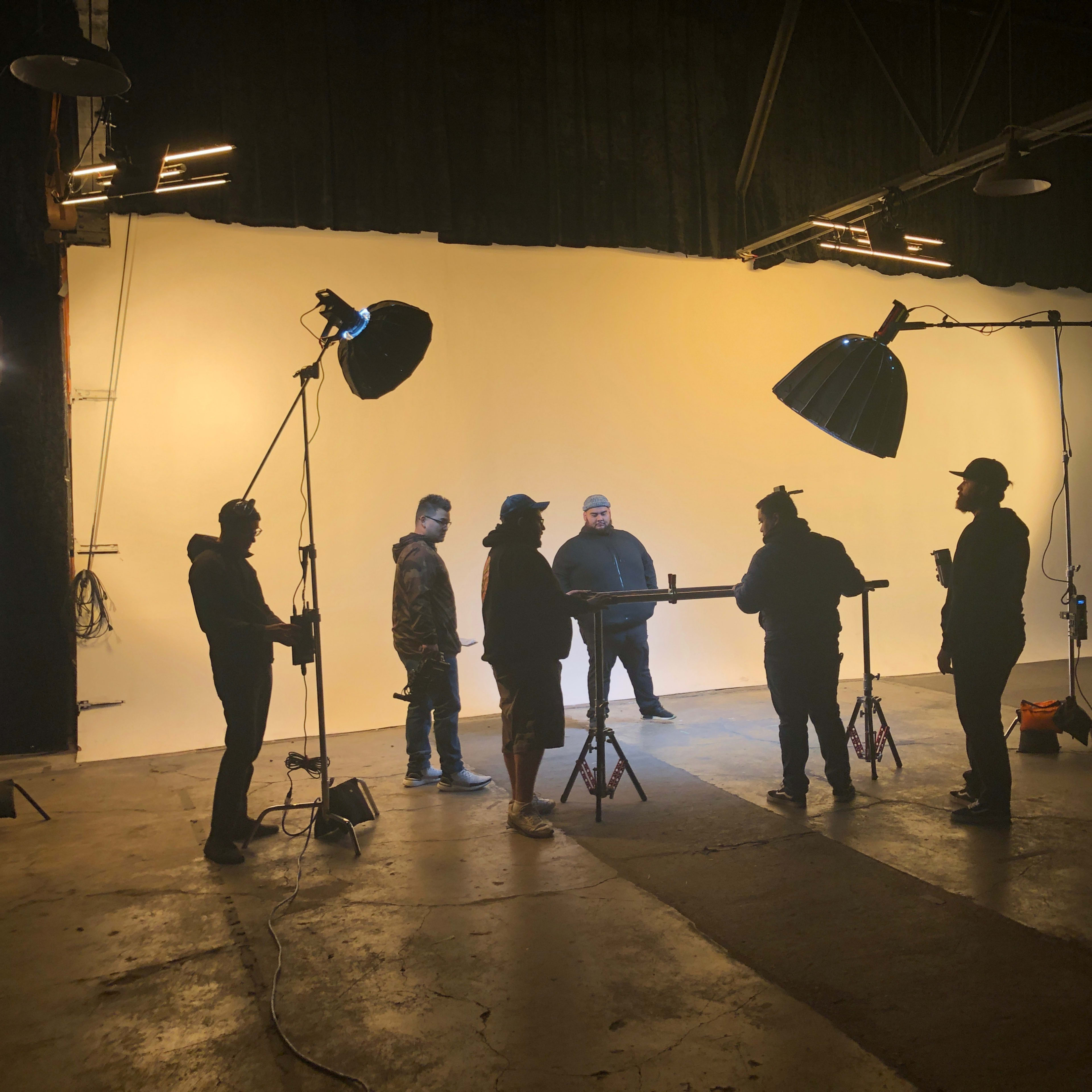 A group of seven people stands in a studio with a bright backdrop, surrounded by lighting equipment.