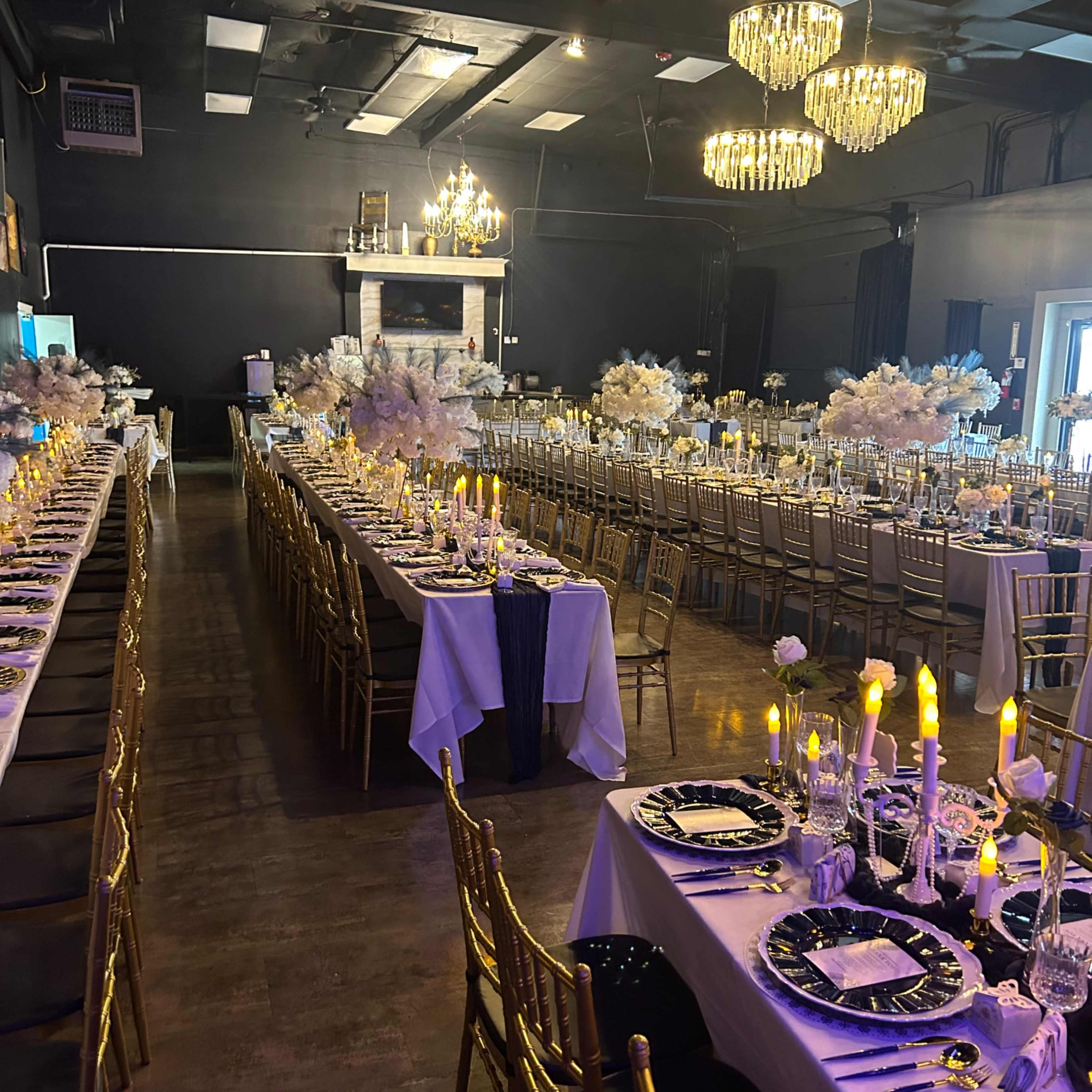 A beautifully set banquet hall featuring long tables arranged with elegant table settings, candles, and floral centerpieces, under sparkling chandeliers.