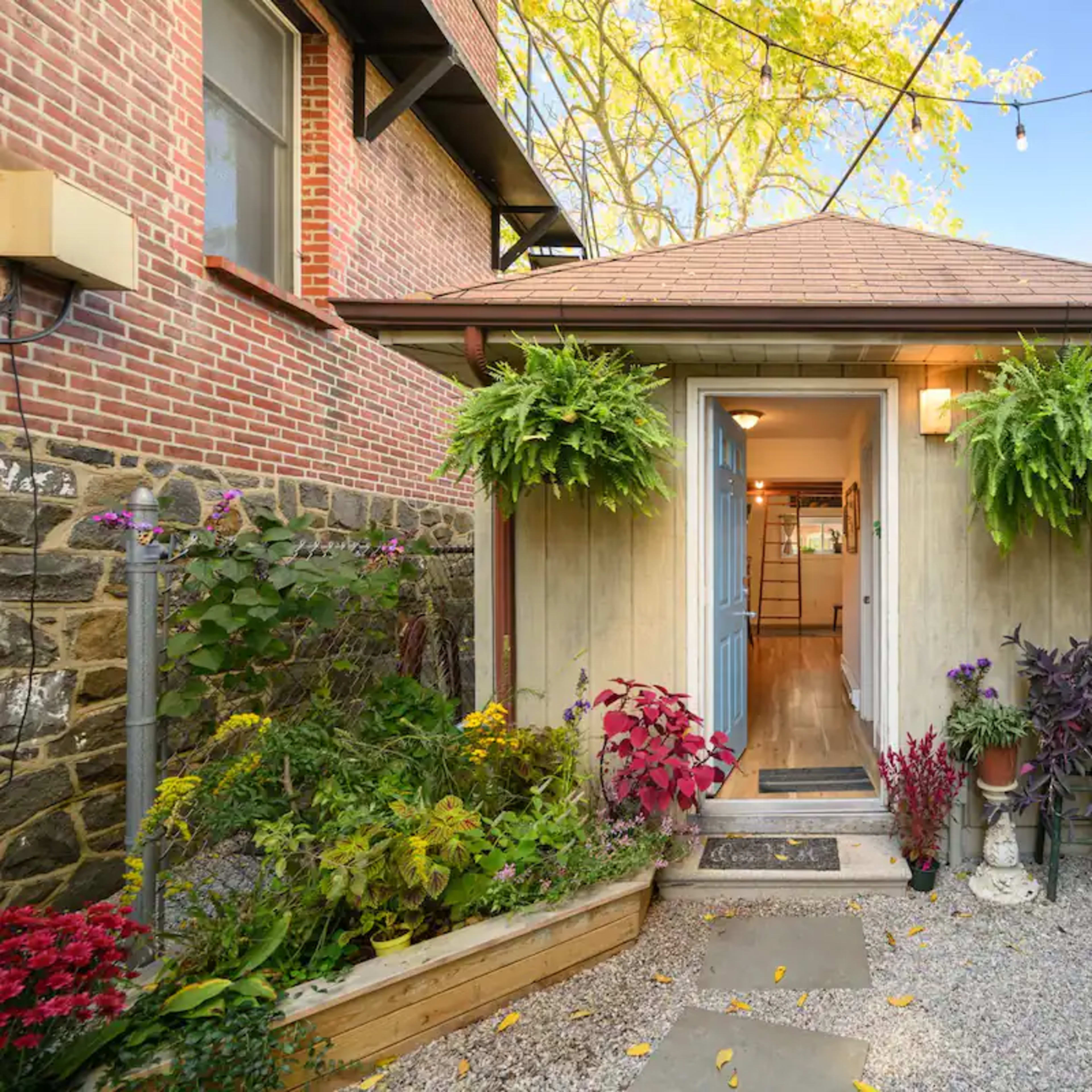 A charming entryway with a pathway leading to a door flanked by hanging plants and surrounded by a gravel garden.