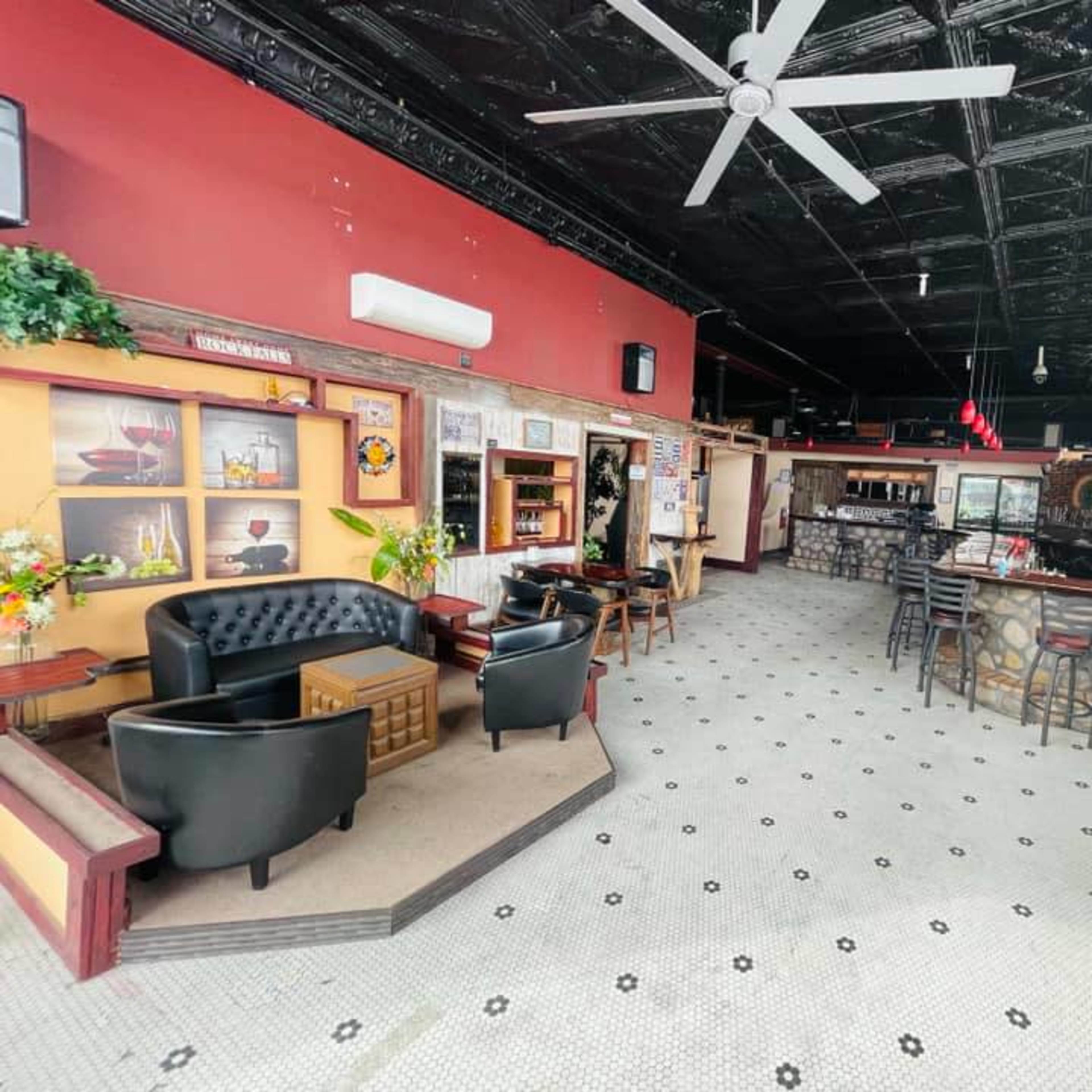 The interior of a restaurant or bar, featuring black leather seating, a stone bar counter, and a tiled floor with a ceiling fan overhead.