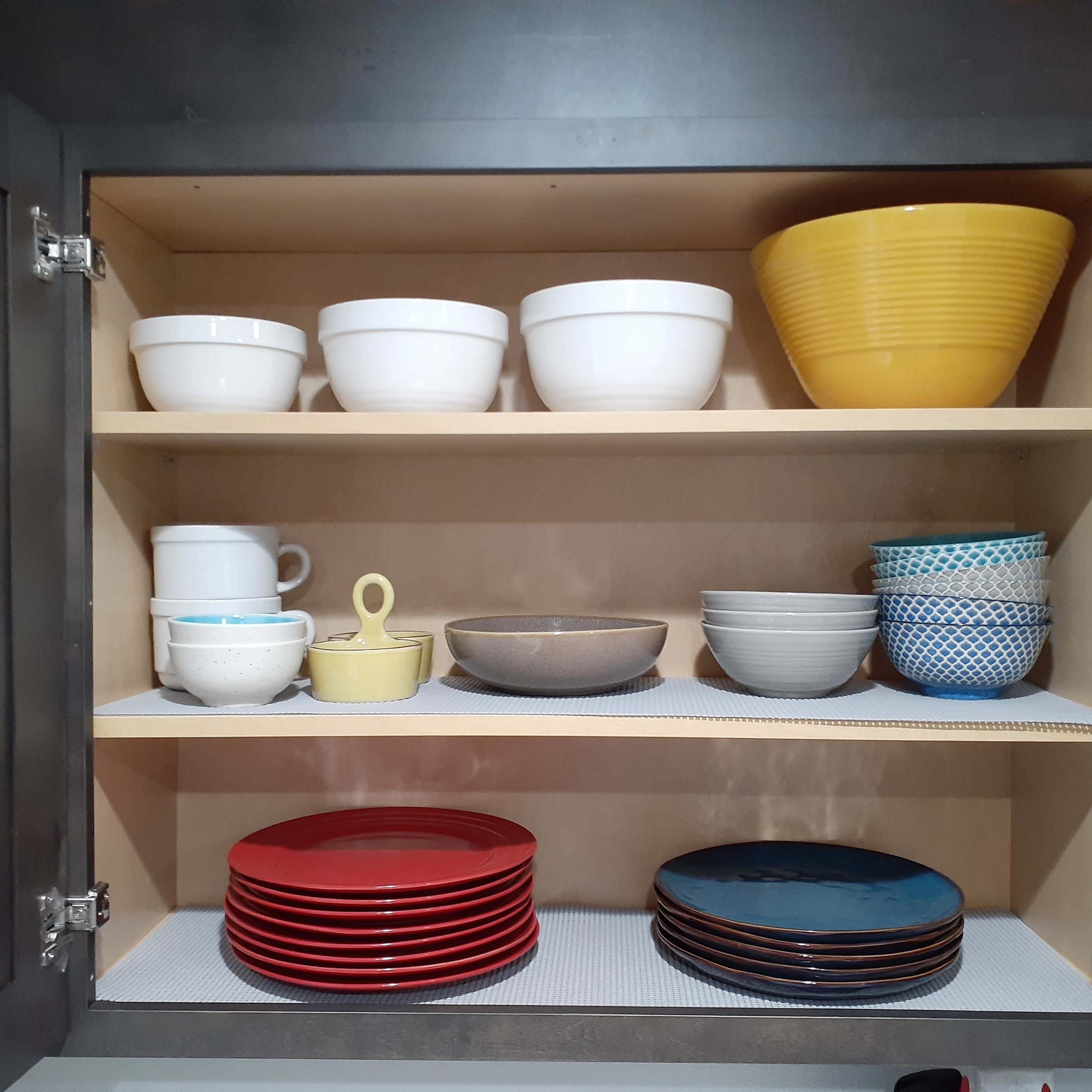 A kitchen cabinet with multiple shelves containing a variety of bowls, plates, and cups organized neatly.