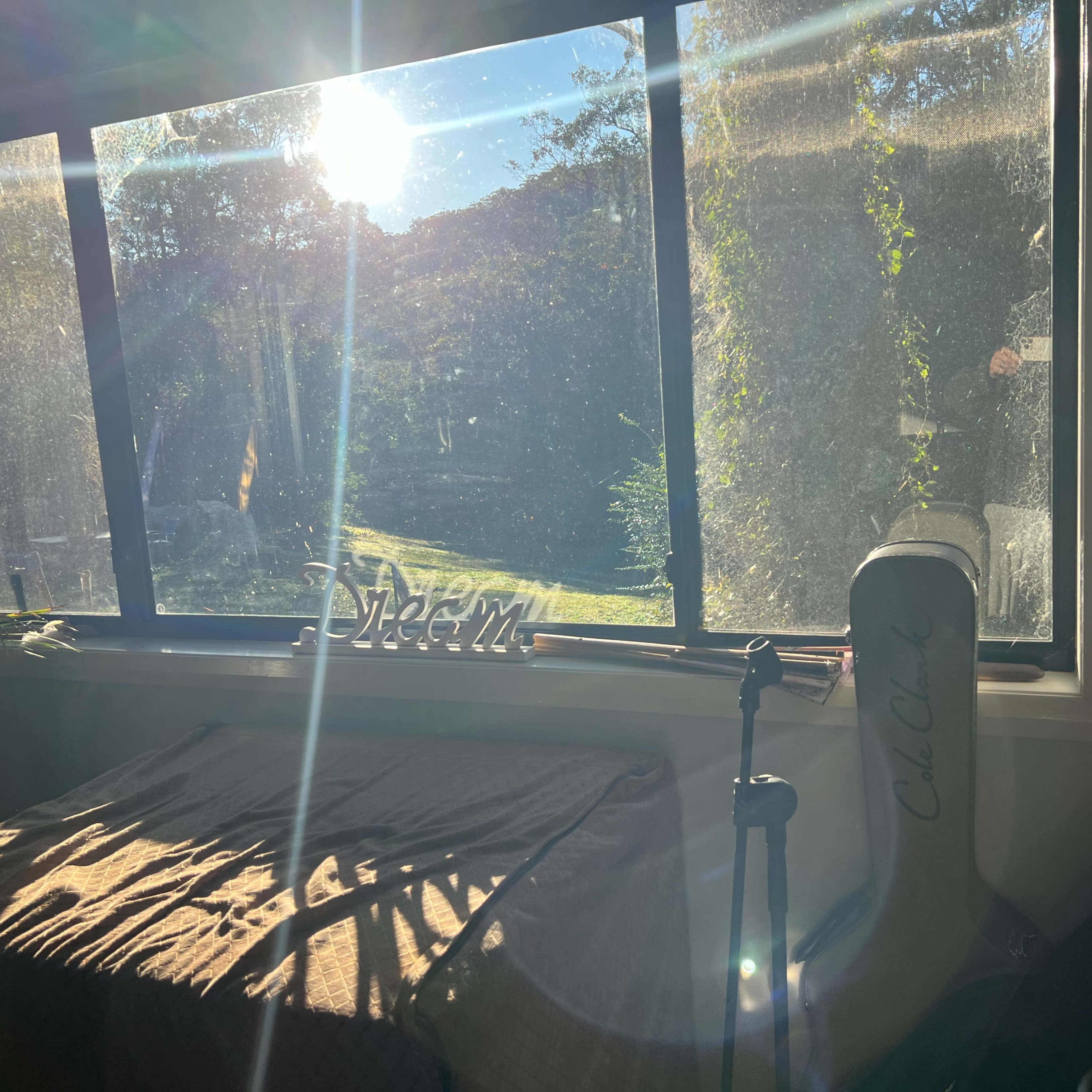 Sunlight streams through a large window, illuminating a room with a table and a chair beside a garden view.