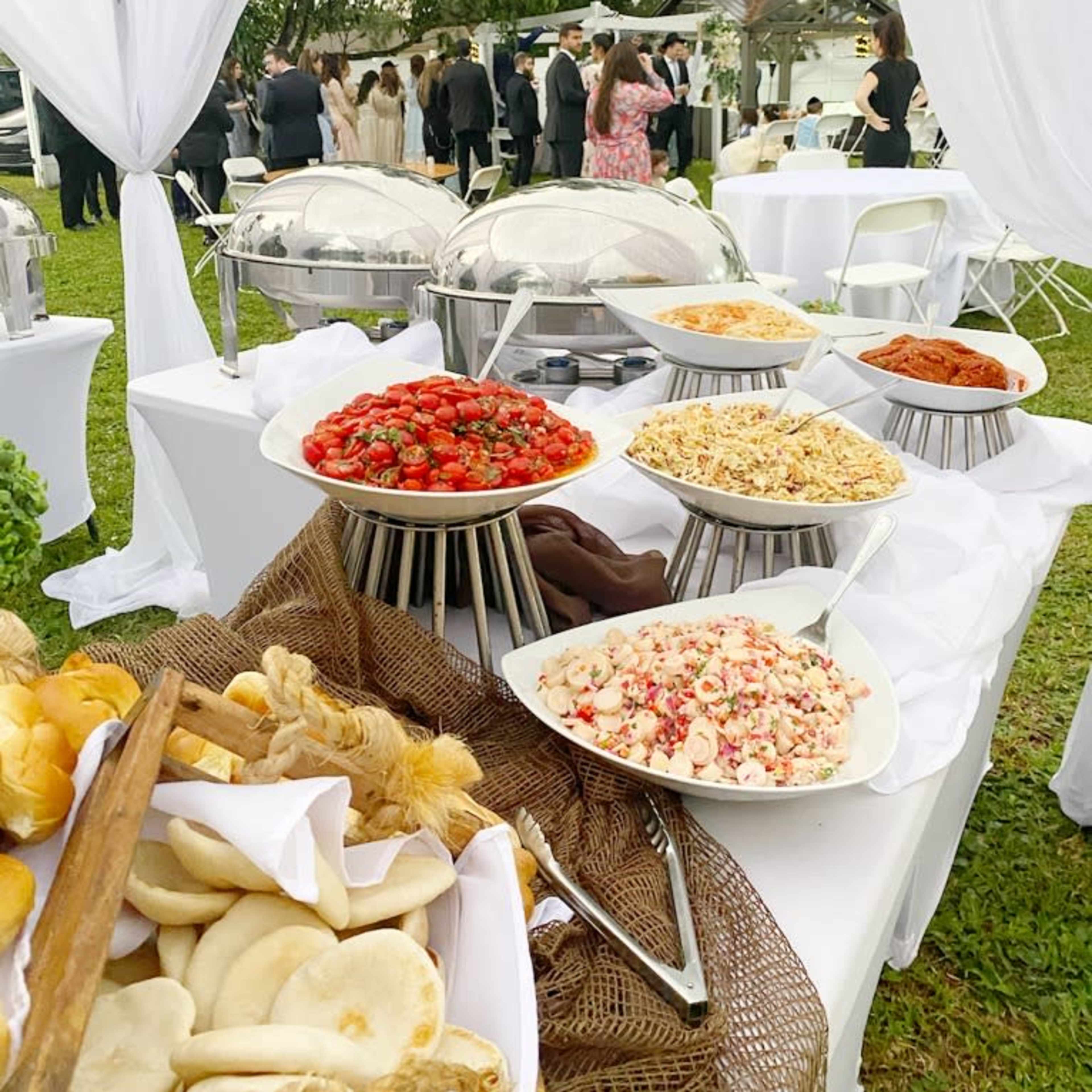 A buffet table displays various dishes, including salads and pastries, set in a garden during an outdoor event.