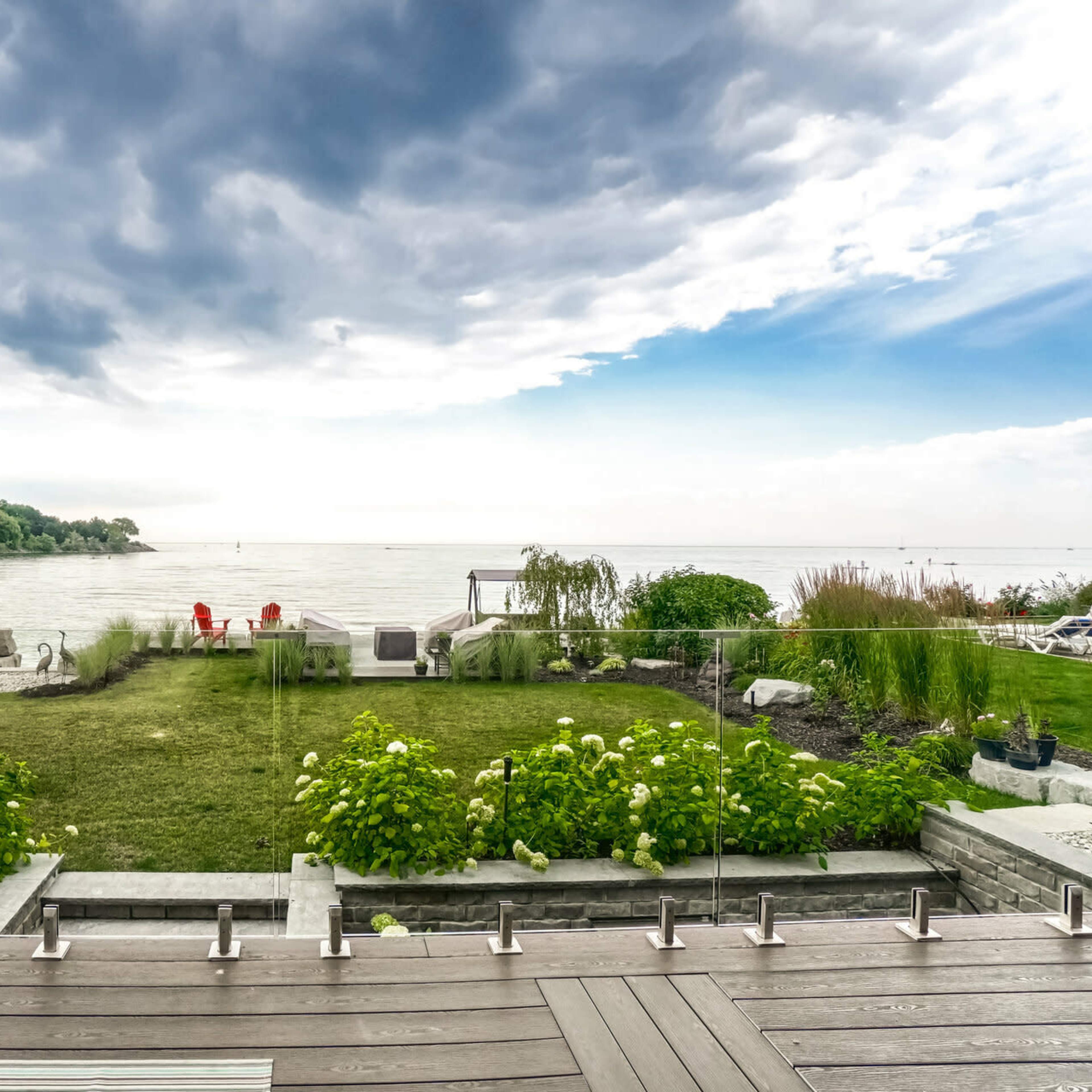 A landscaped garden with green grass and plants overlooks a calm body of water under a cloudy sky.
