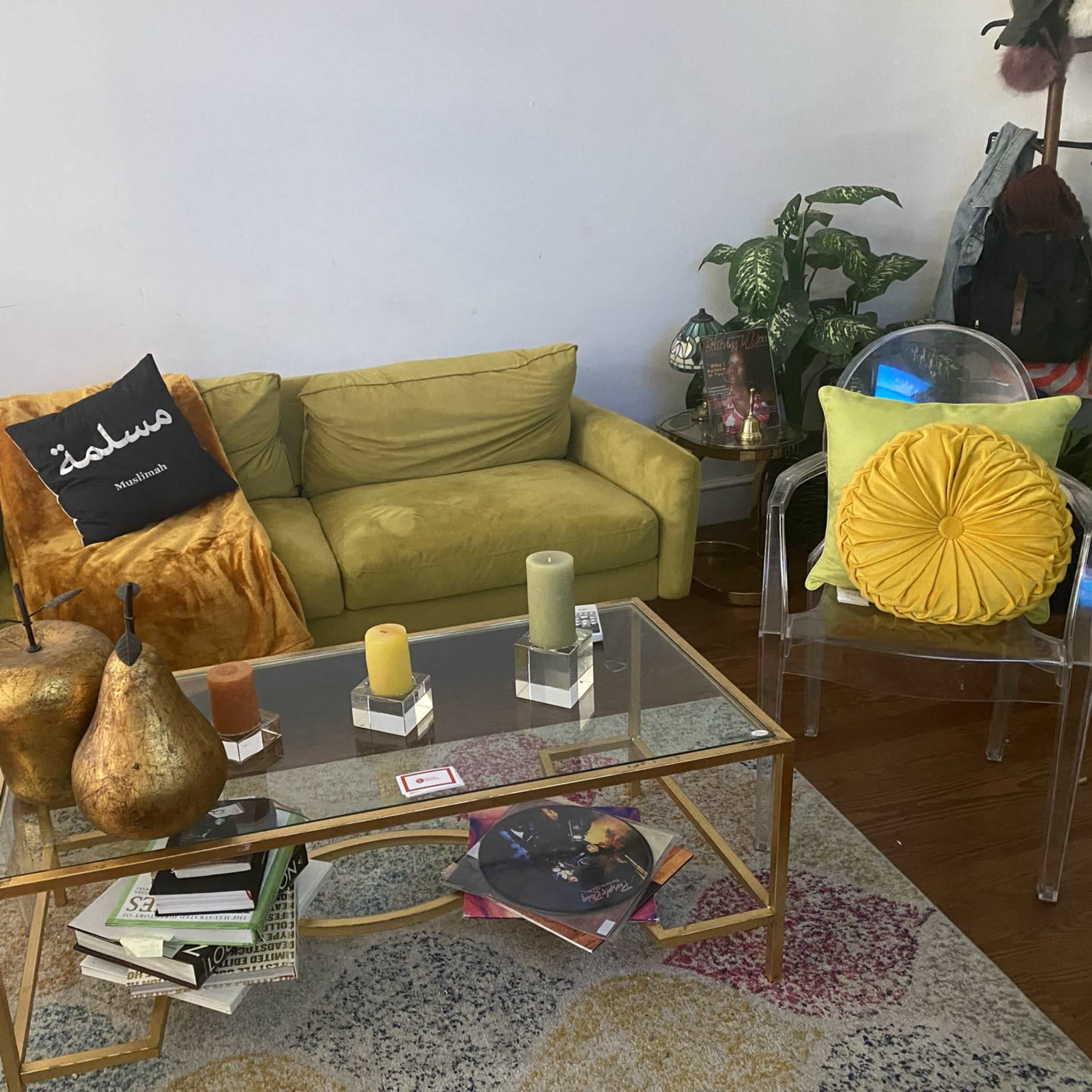 A living room with a bright green sofa, yellow accent pillows, a glass coffee table with decorative items, and indoor plants.