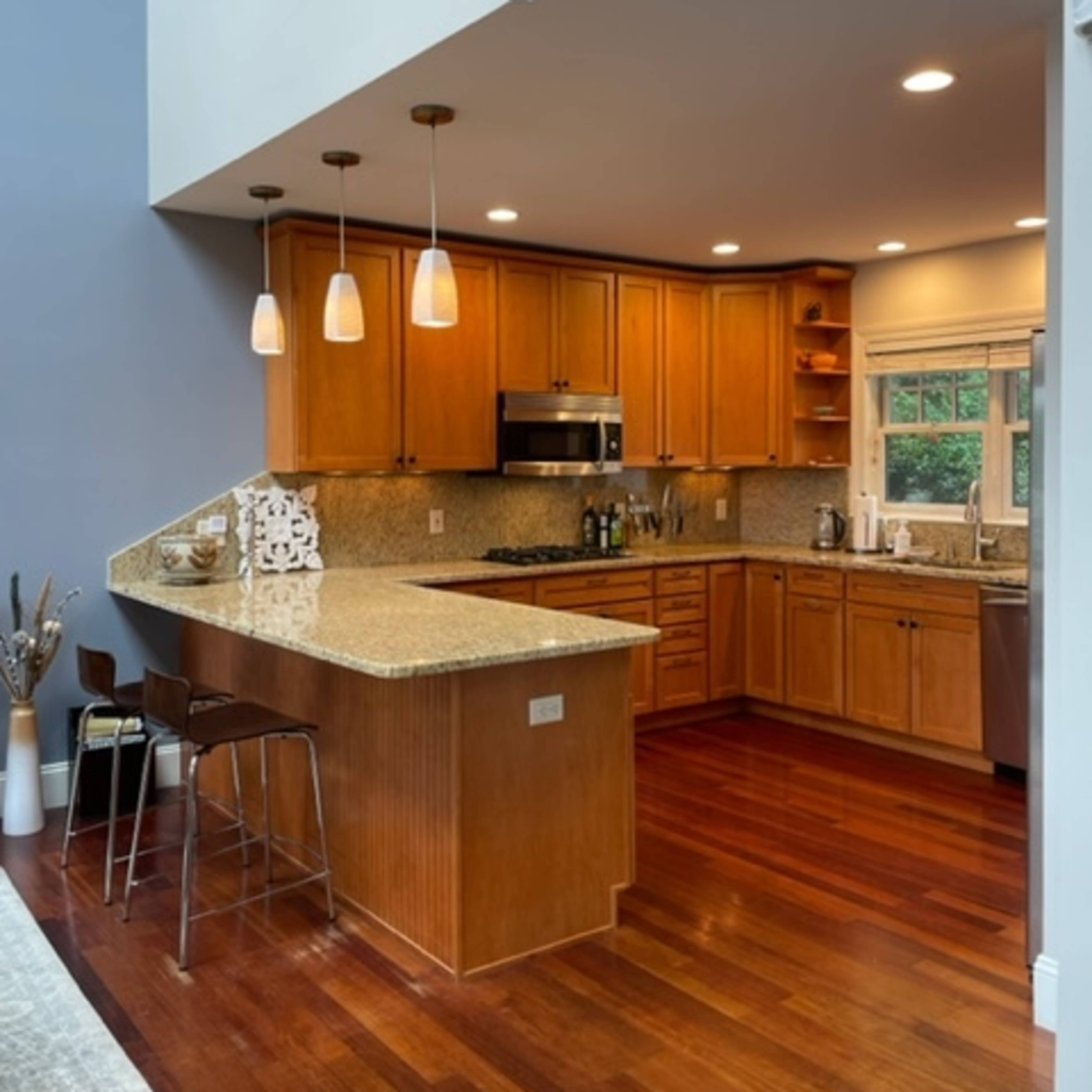 A modern kitchen with wooden cabinetry, granite countertops, and pendant lighting above a counter with barstools.