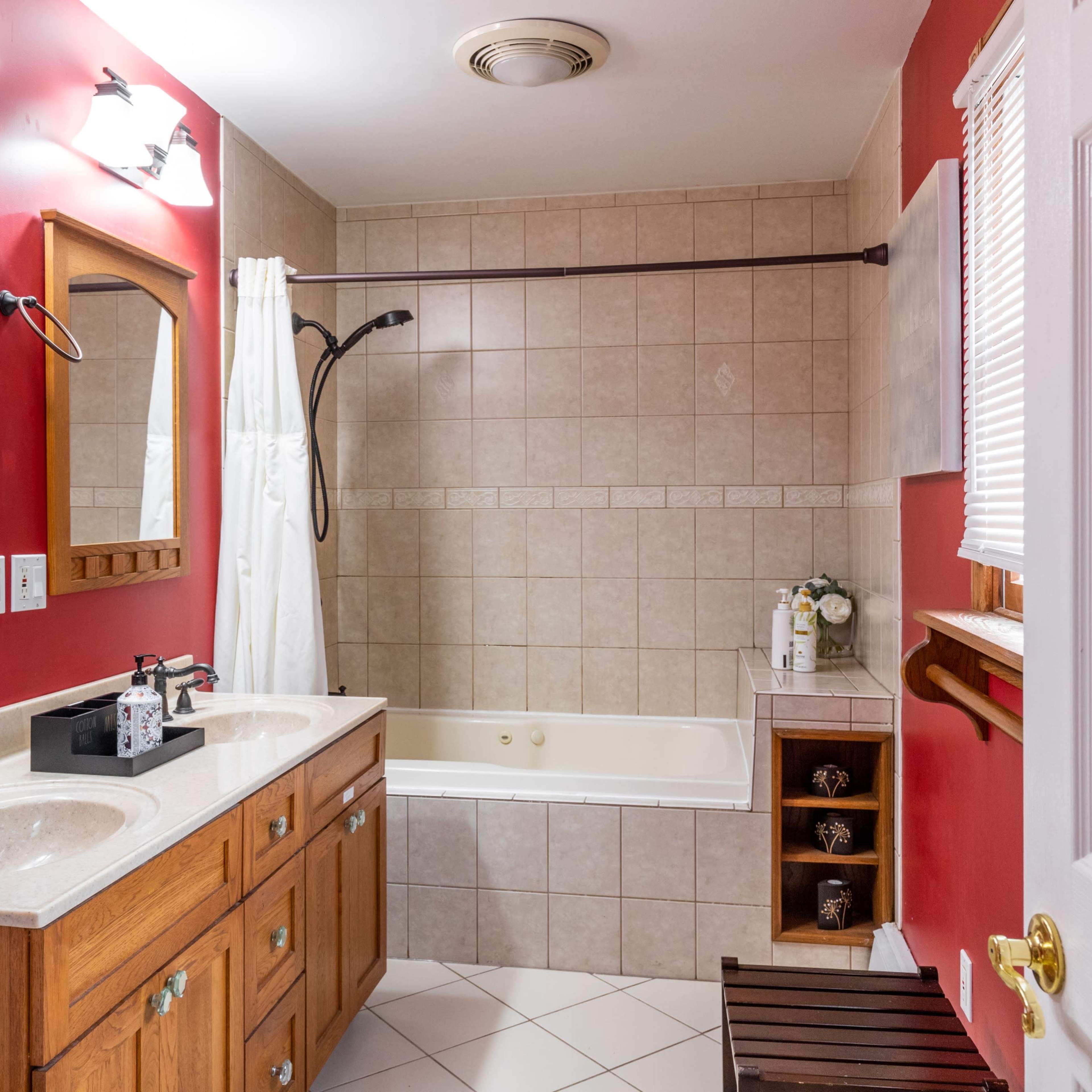 The bathroom features a double sink vanity with wooden cabinetry, a bathtub next to a shower area, and red walls with tiled accents.