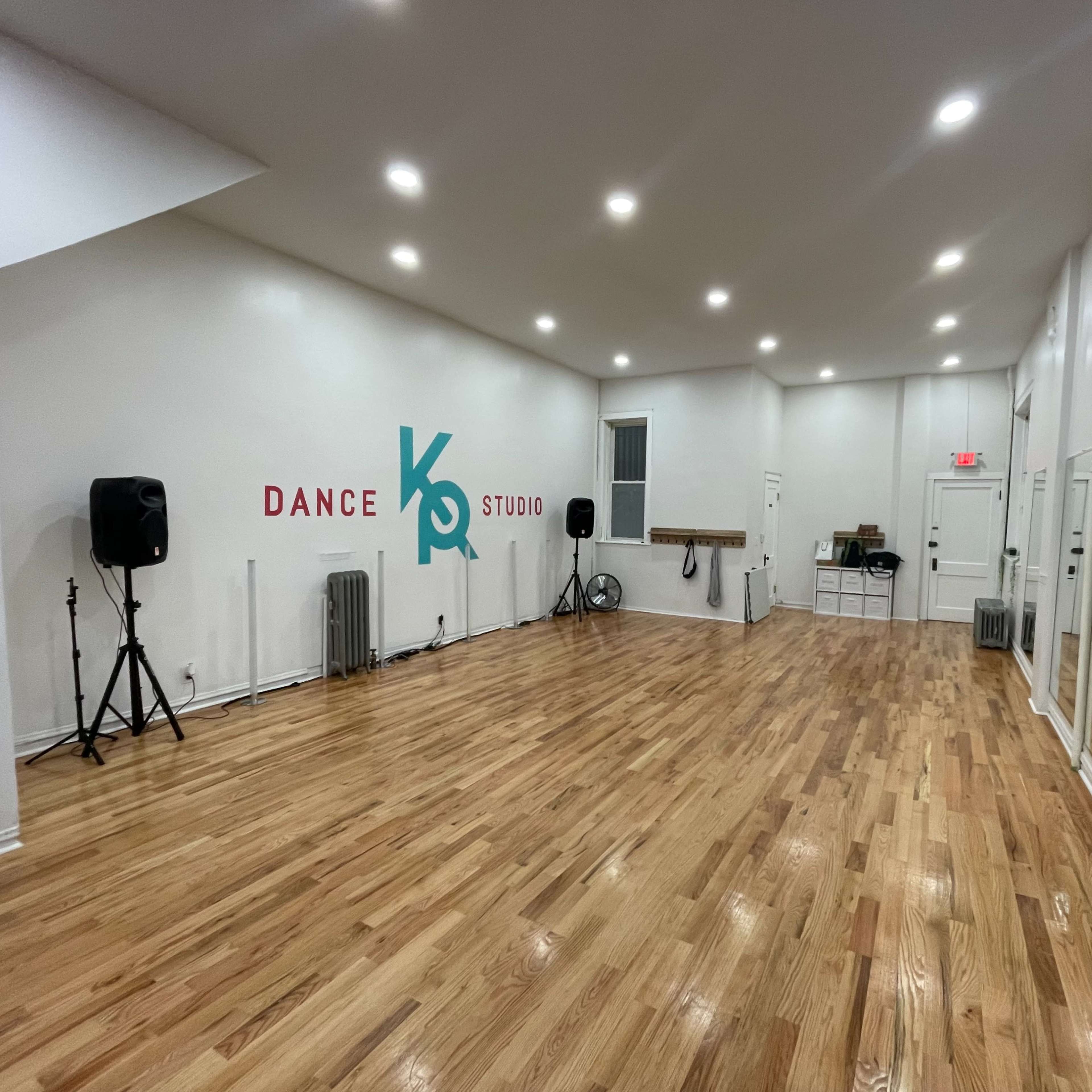A spacious dance studio with wooden flooring, mirrors on one wall, and a colorful wall design that reads "DANCE STUDIO."