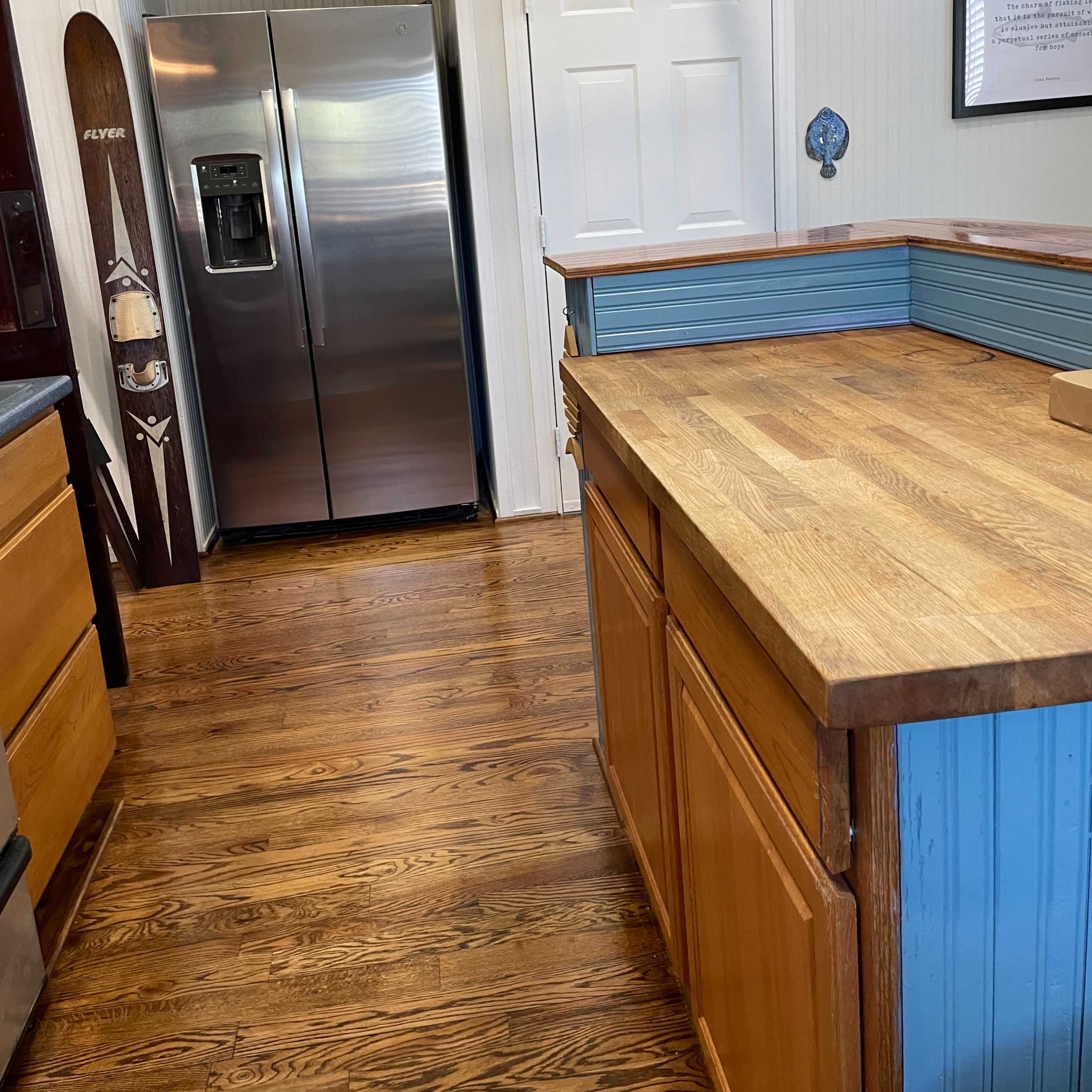 A kitchen with wooden cabinets and a countertop facing a stainless steel refrigerator in a corner.