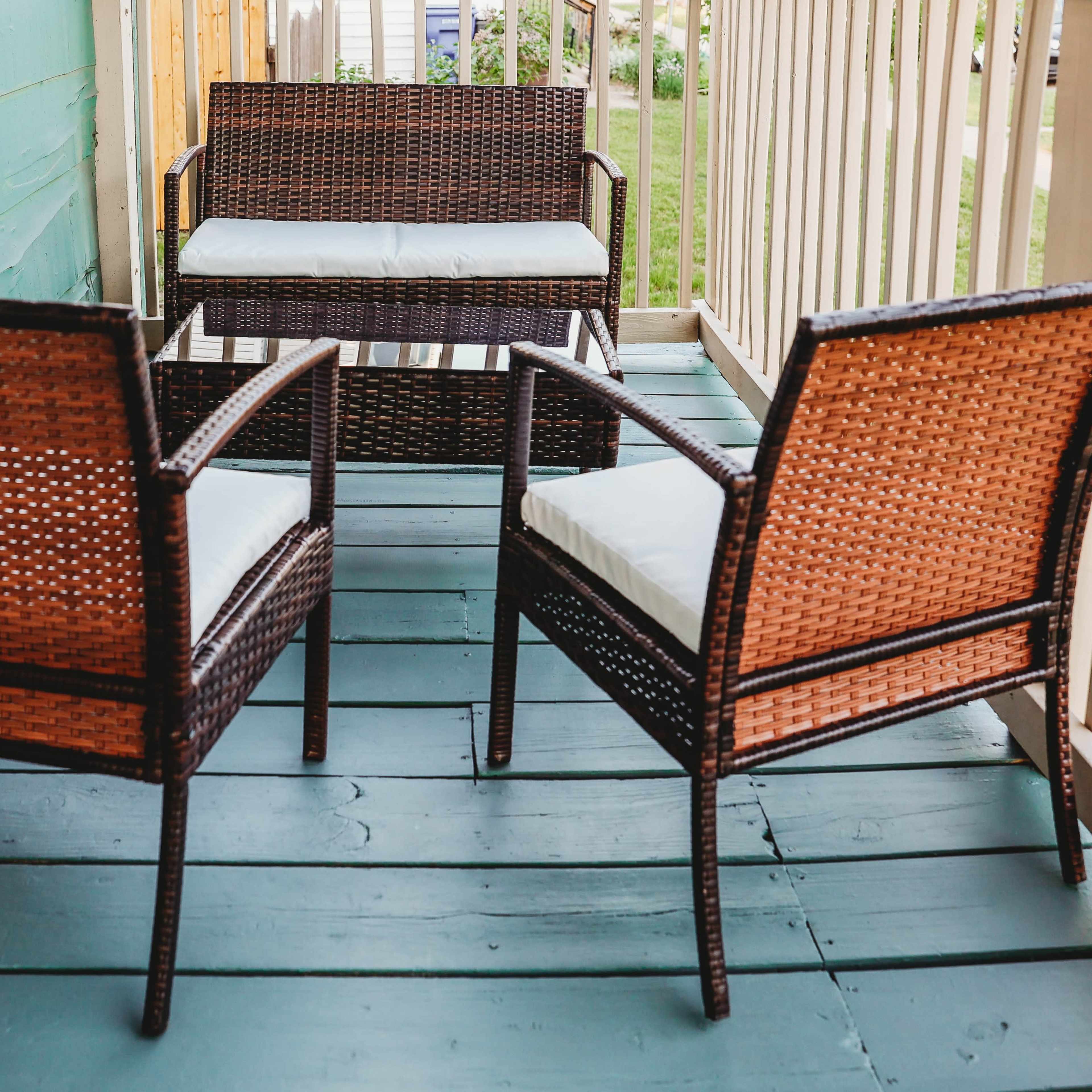 A seating arrangement on a porch, featuring two armchairs and a small loveseat, all made of woven material and placed on a teal wooden floor.