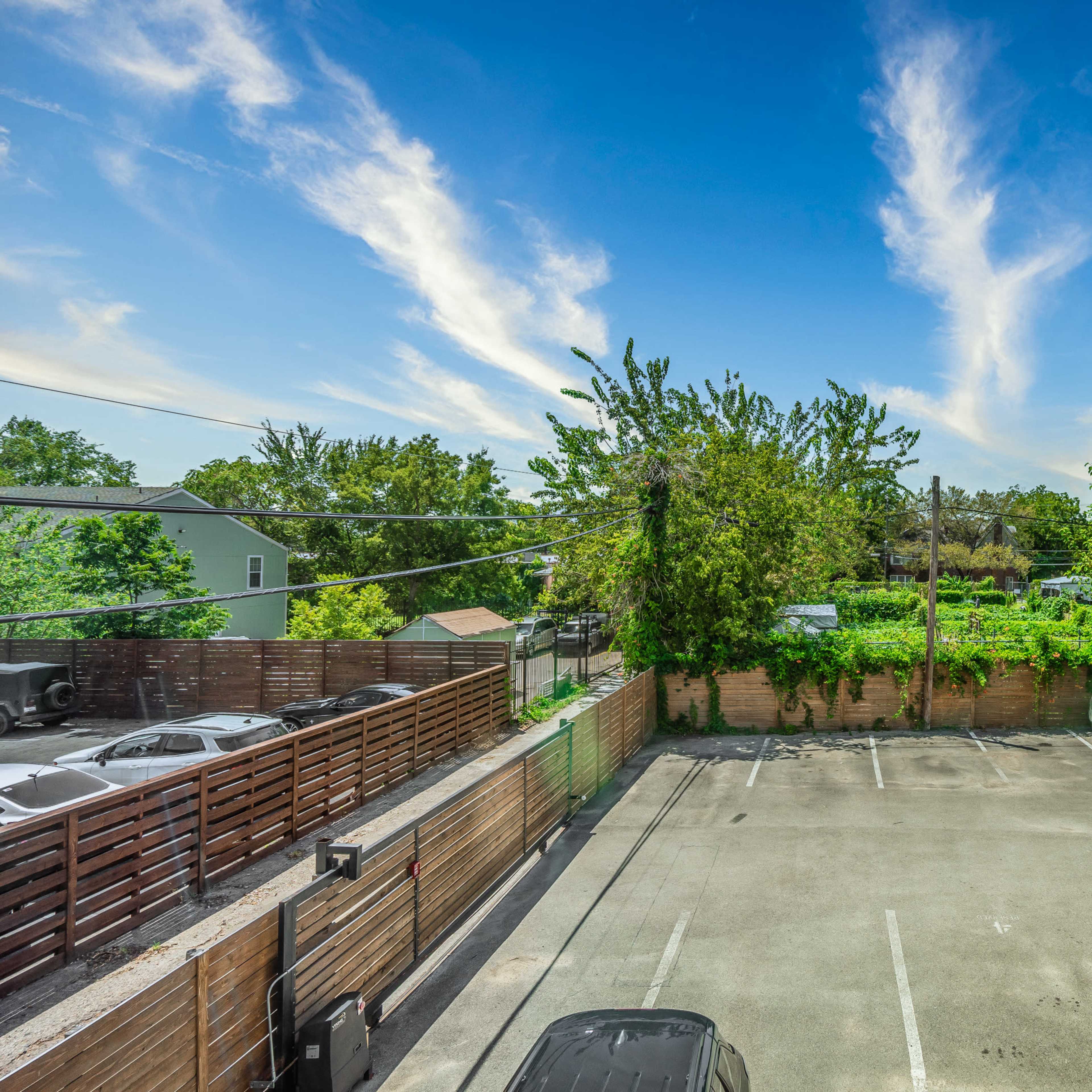 An open parking lot with several parked cars surrounded by trees and a clear blue sky.