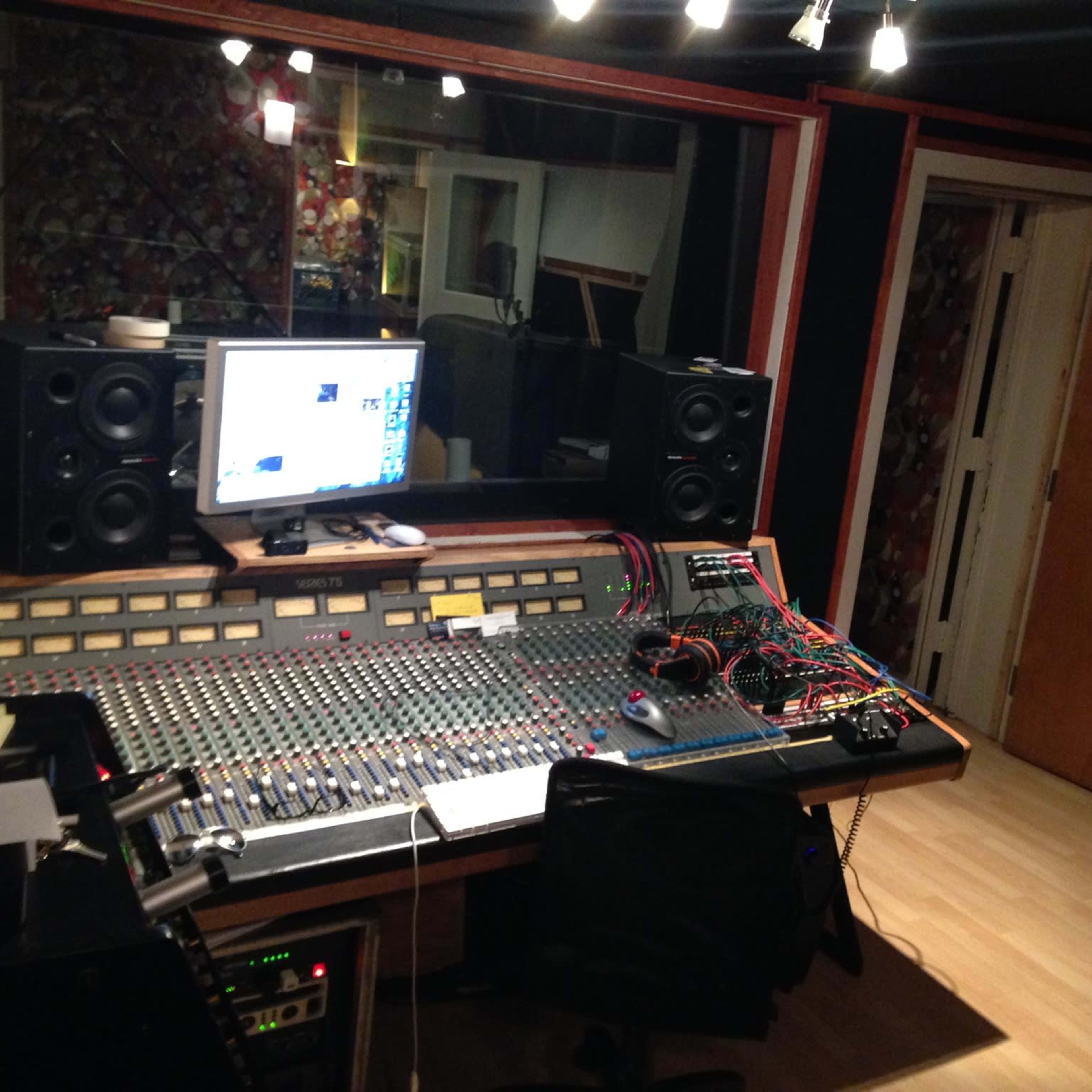 A recording studio with a large mixing console, computer monitor, and various audio equipment, surrounded by soundproofing materials.