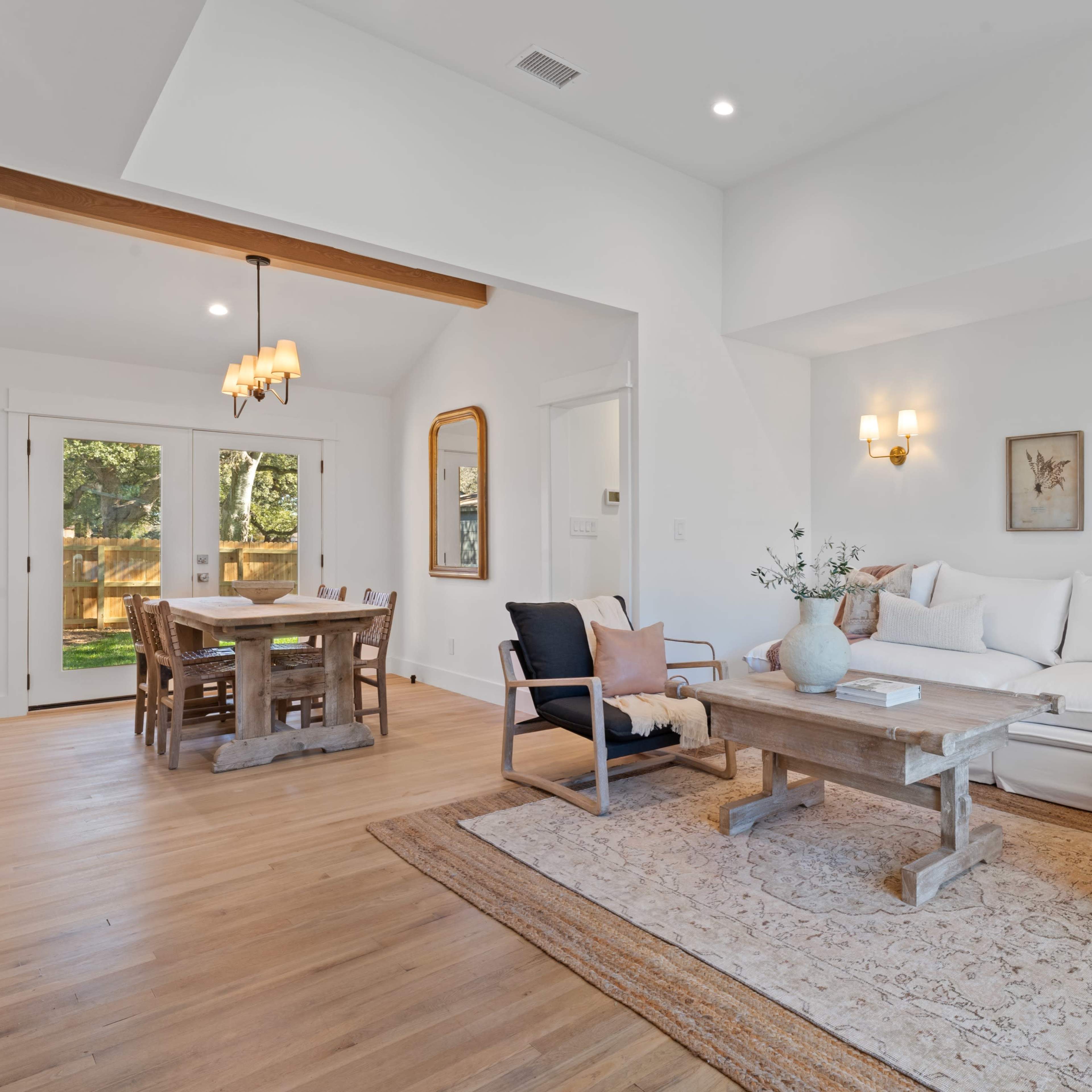 A bright, modern living room with a large white sectional sofa, a wooden coffee table, and a dining area with a wooden table set for six.