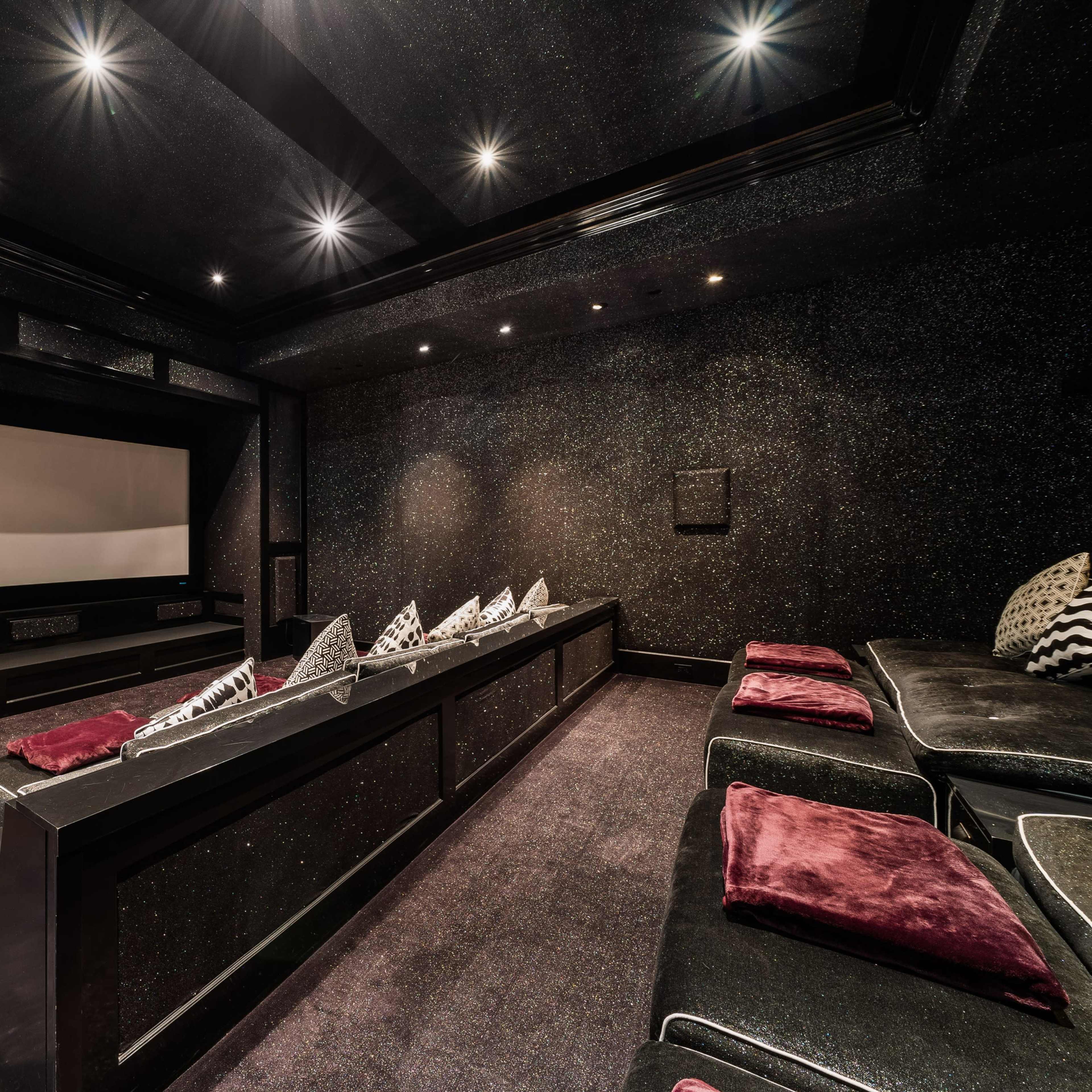 A dimly lit home theater with a large projector screen, tiered seating, and plush cushions.