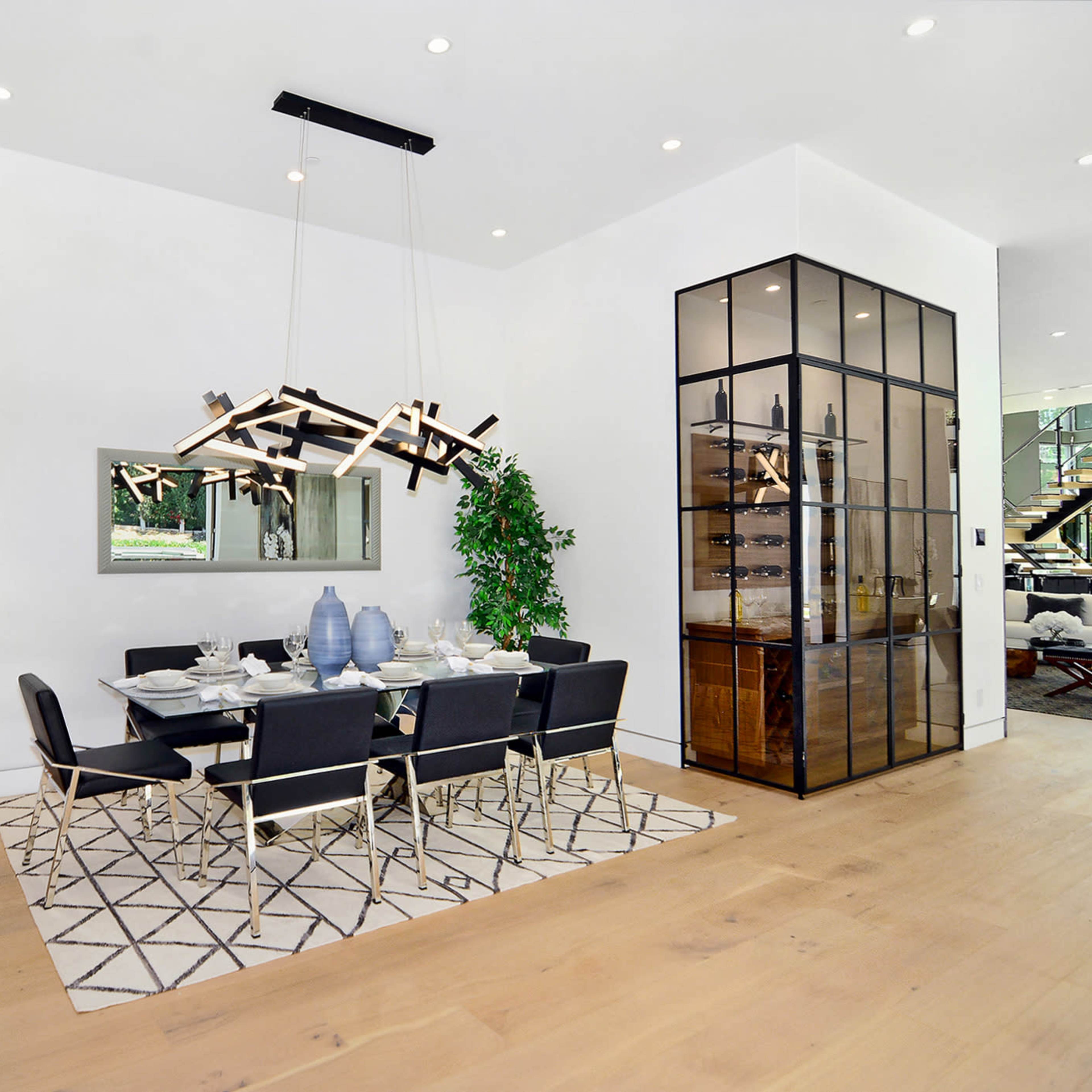 A modern dining area features a rectangular table with black chairs, a stylish light fixture above, and a glass cabinet in the background.