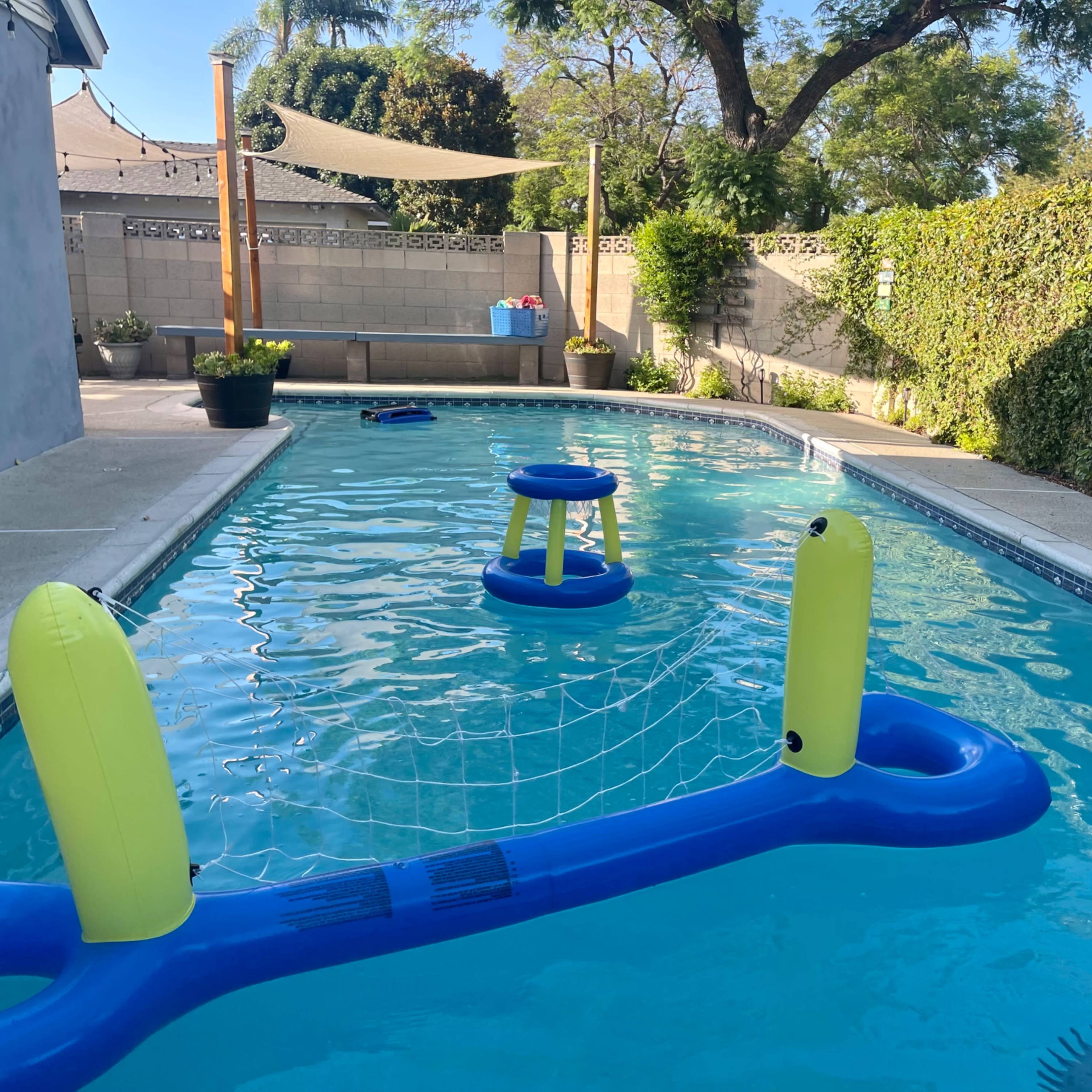 A swimming pool with a floating volleyball net and two inflatable chairs on the water.