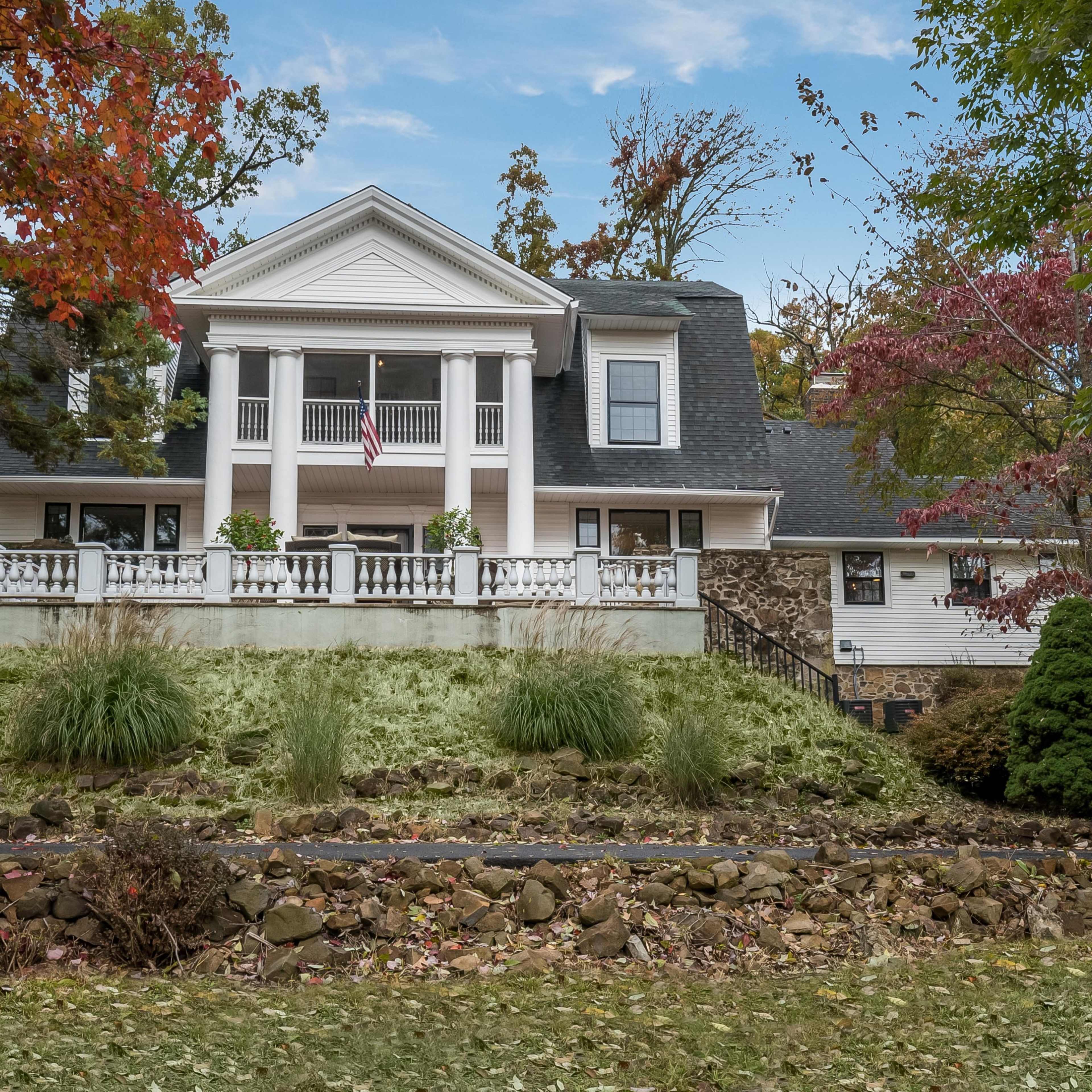A two-story house with a front porch, surrounded by trees and landscaped grounds, is located on a grassy hillside.