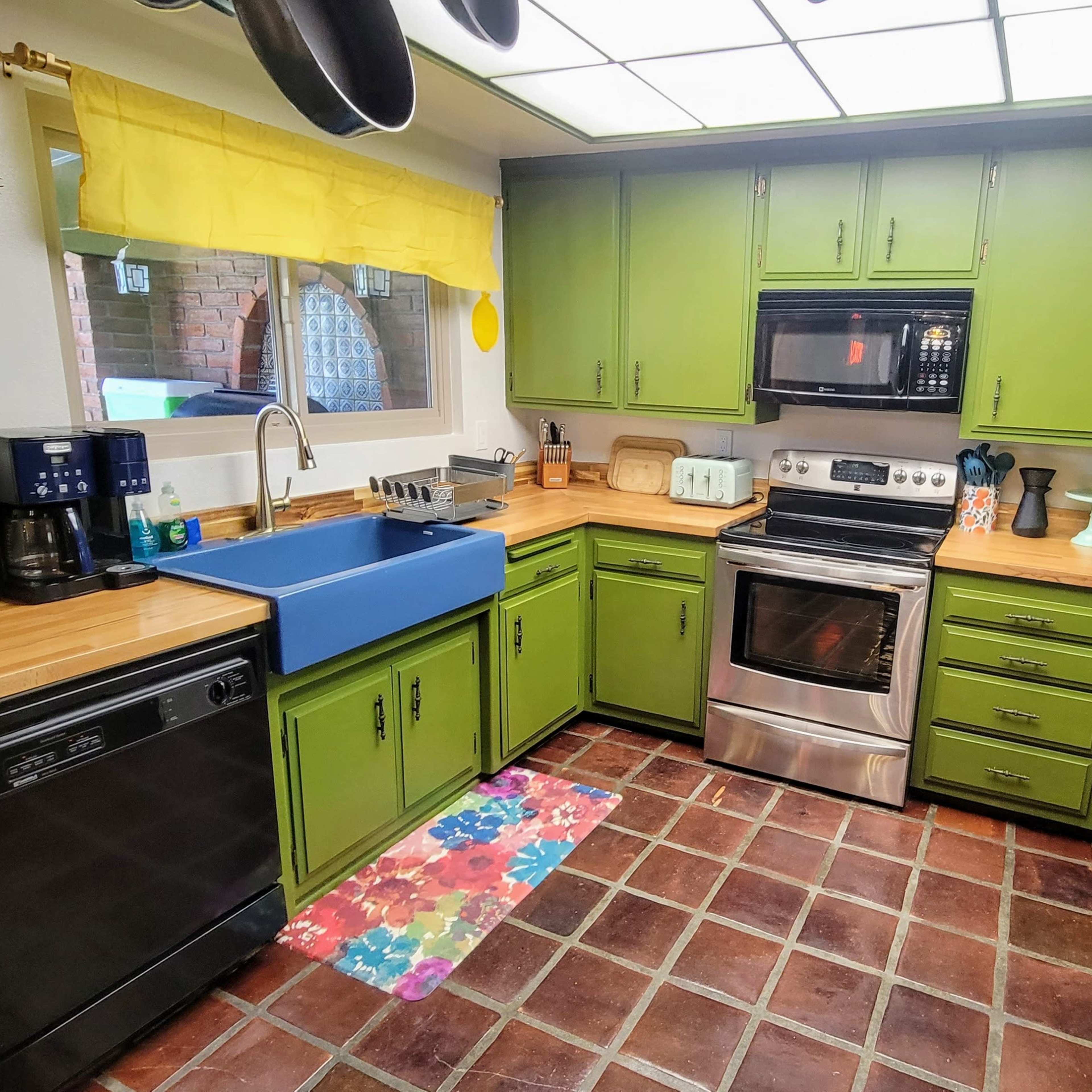 The kitchen features green cabinetry, a stainless steel oven, and a blue sink, with tile flooring and a colorful floral mat.