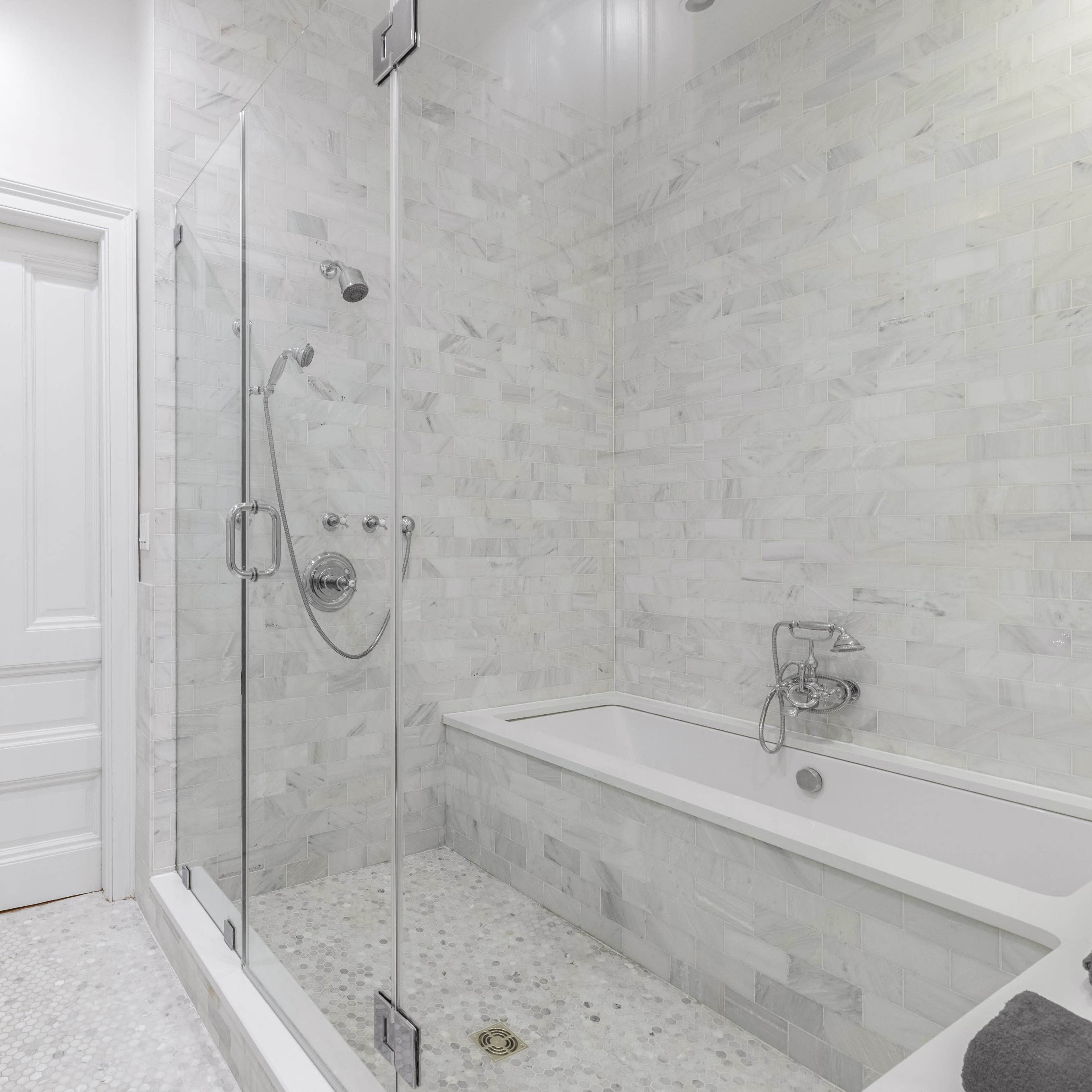 A modern bathroom featuring a glass shower enclosed by marble walls and a freestanding bathtub.
