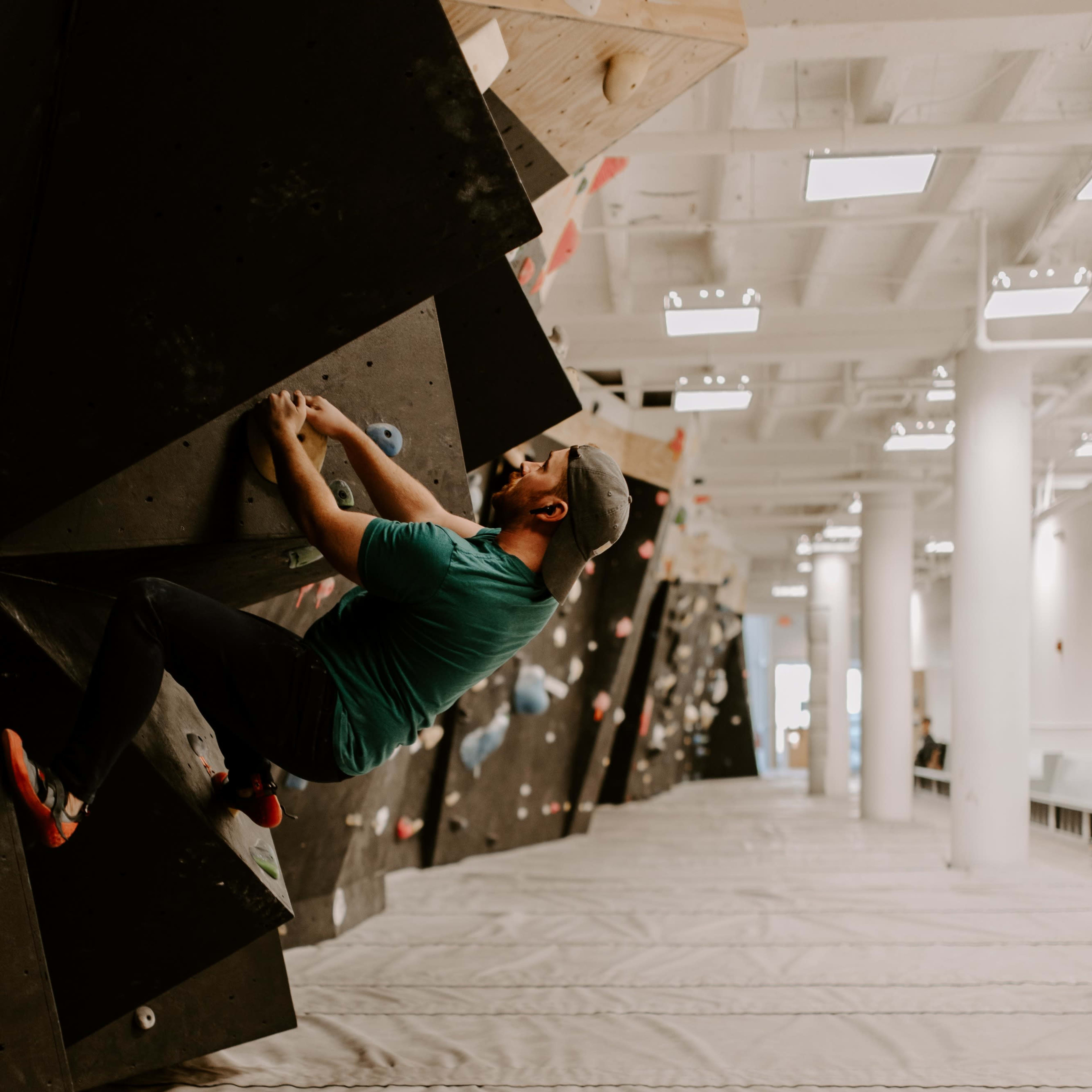 A climber scales a steep, angular bouldering wall in an indoor climbing gym.