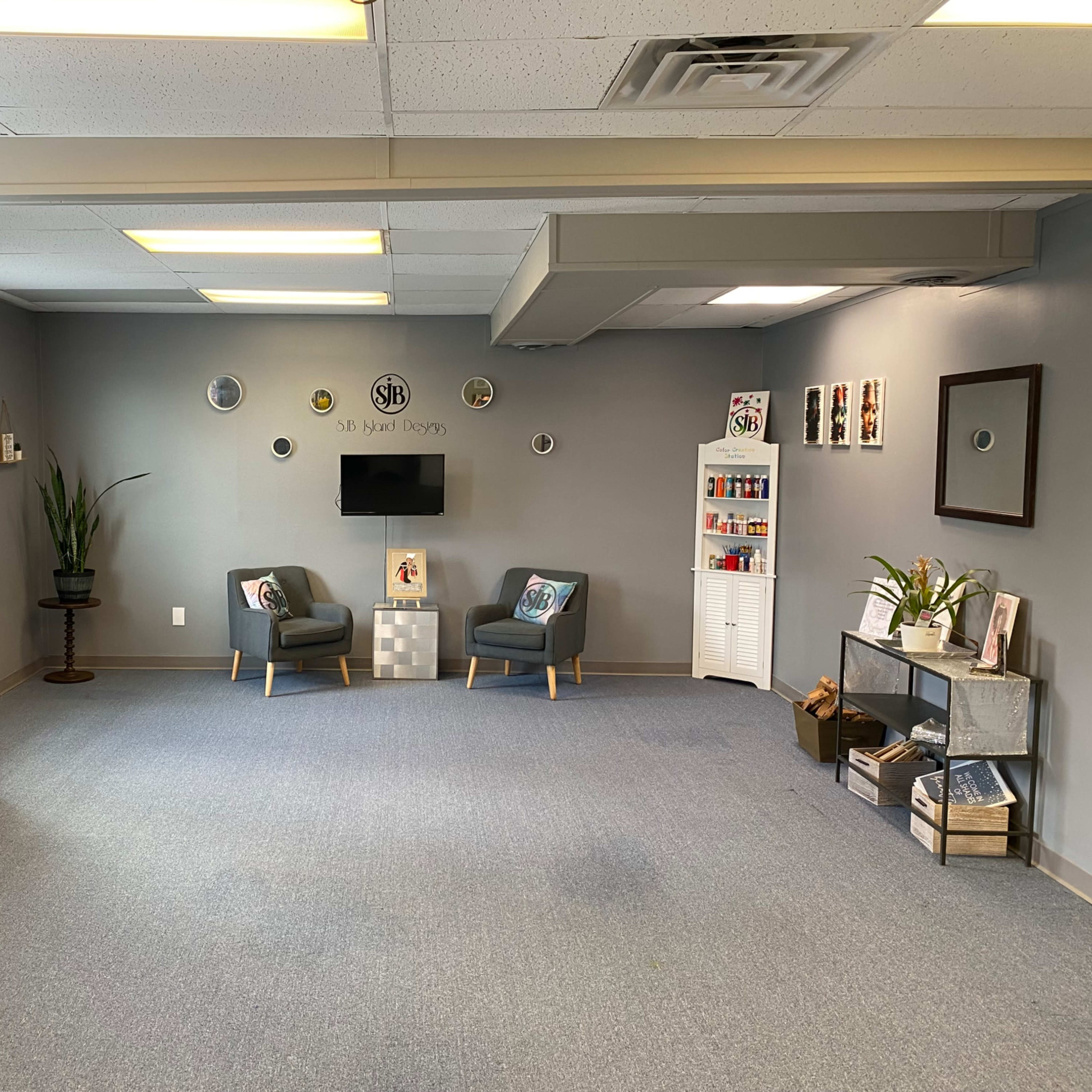 A spacious room with gray walls, two chairs, a small table, a television on the wall, and decorative items displayed on shelves.