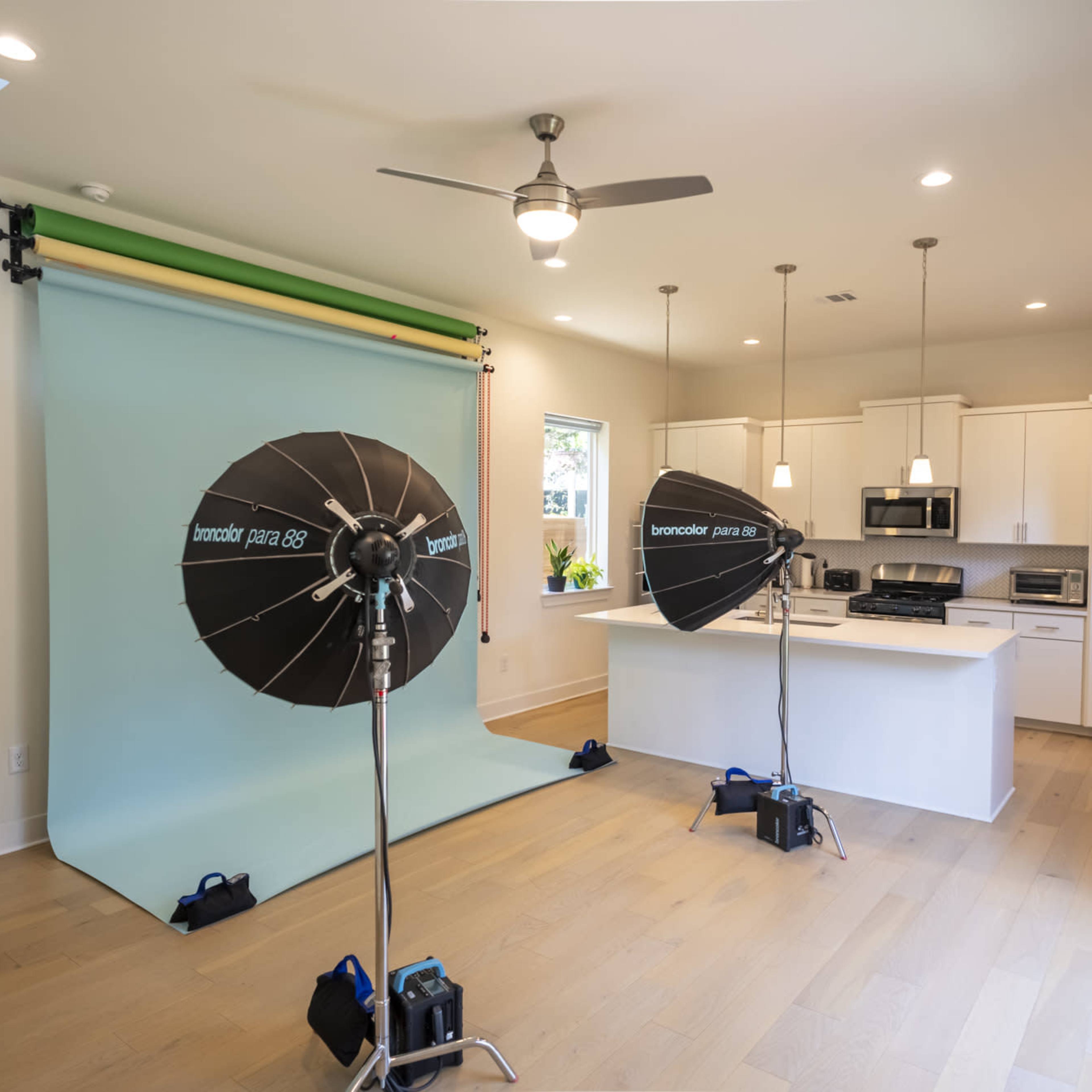 A kitchen with a green and blue backdrop set up for photography, featuring softbox lights and modern appliances.