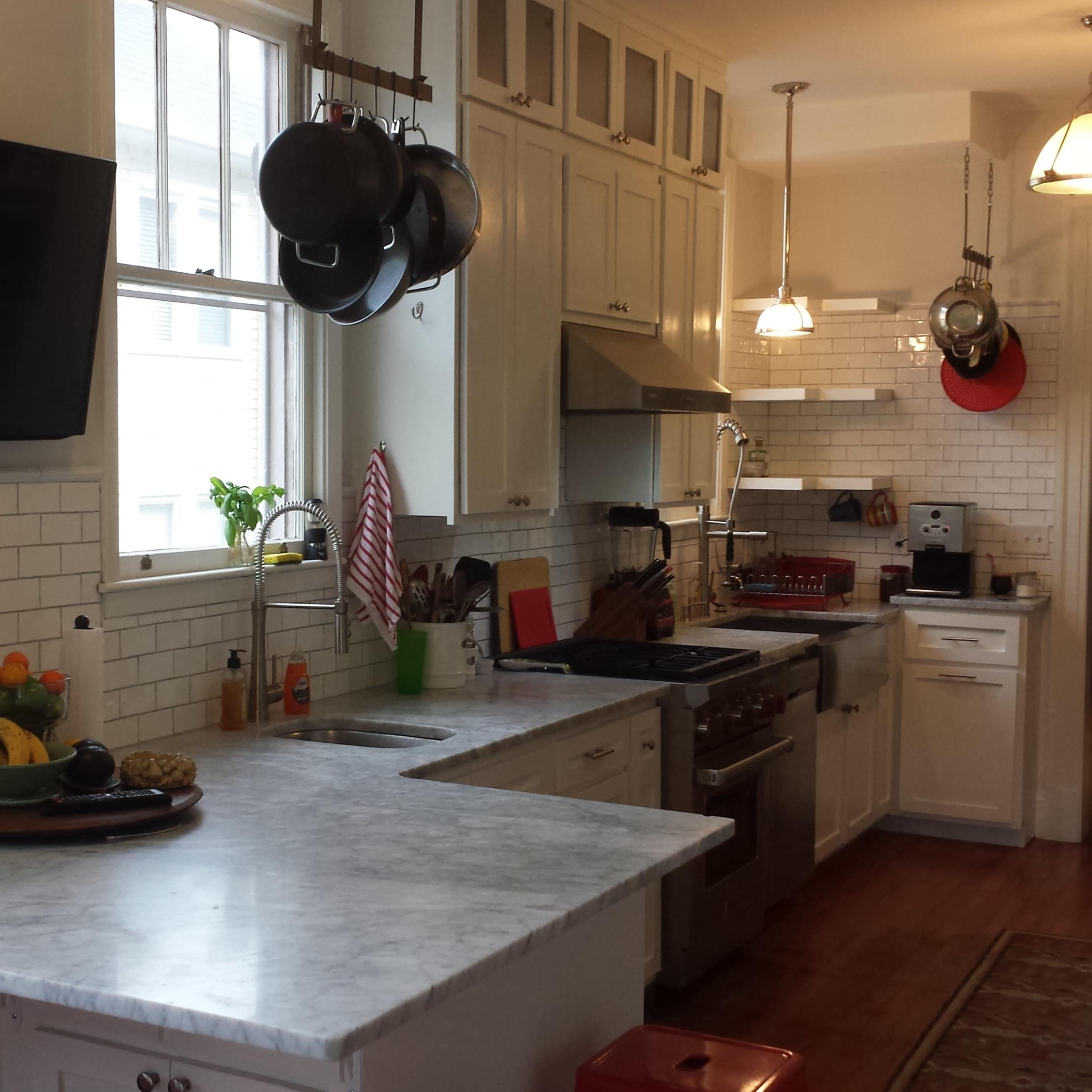 A modern kitchen featuring marble countertops, stainless steel appliances, and a television mounted on the wall.