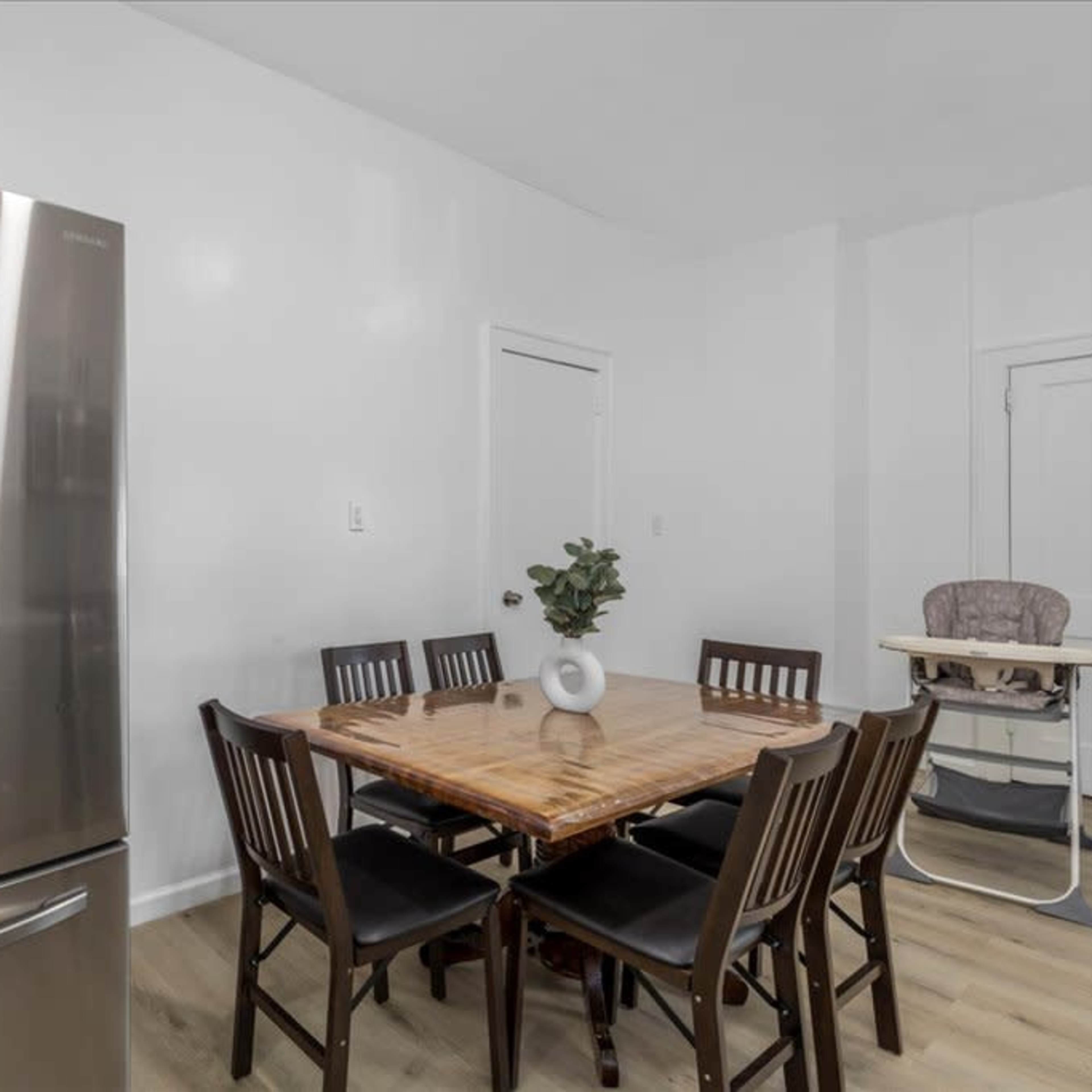 A modern kitchen features a stainless steel refrigerator next to a wooden dining table surrounded by eight chairs.