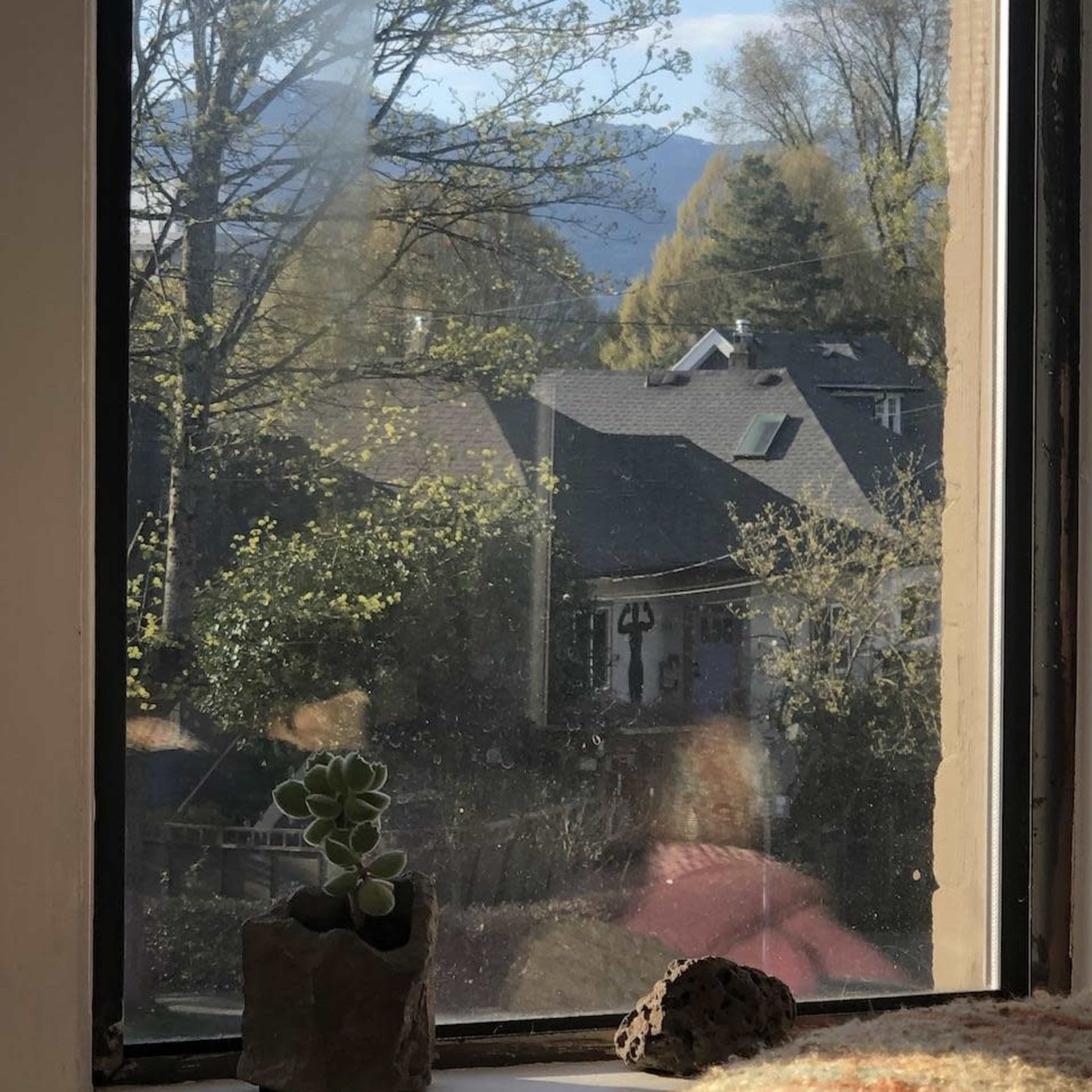 A view from a window overlooking rooftops, trees, and distant mountains under a clear sky.