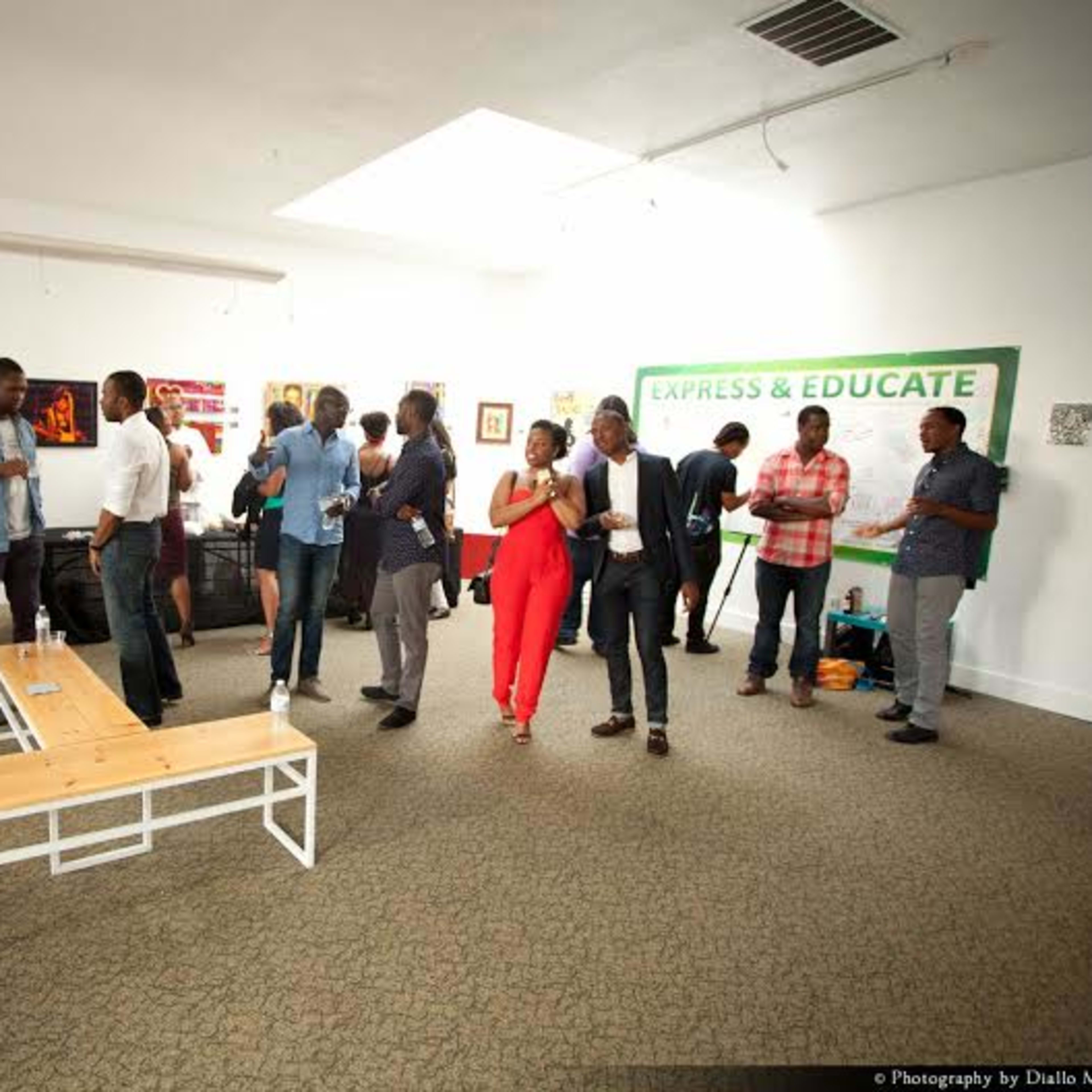 A group of people mingles in an art gallery adorned with various artworks and a large sign that reads "EXPRESS & EDUCATE."