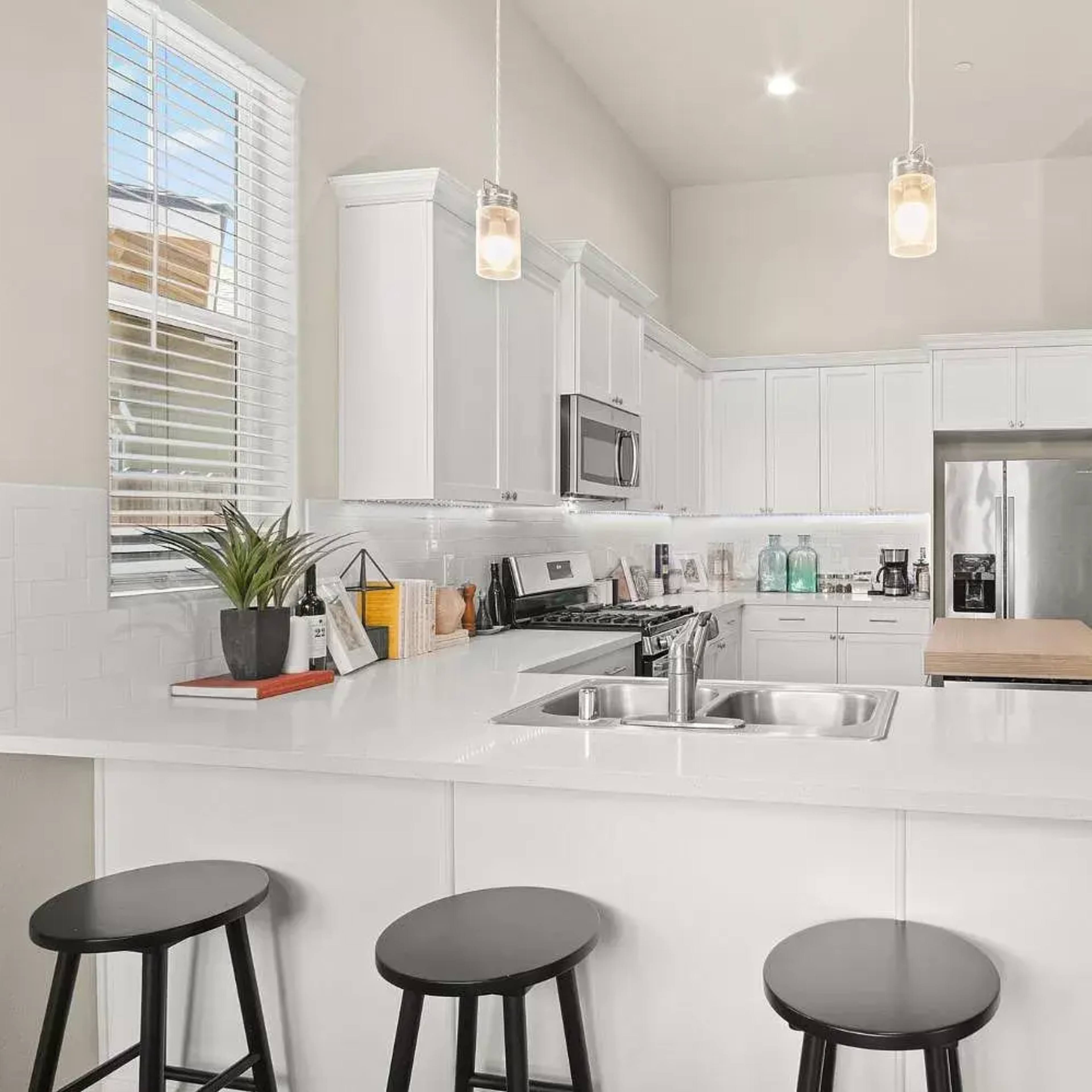 A modern kitchen with white cabinetry, a large island with bar stools, and stainless steel appliances.