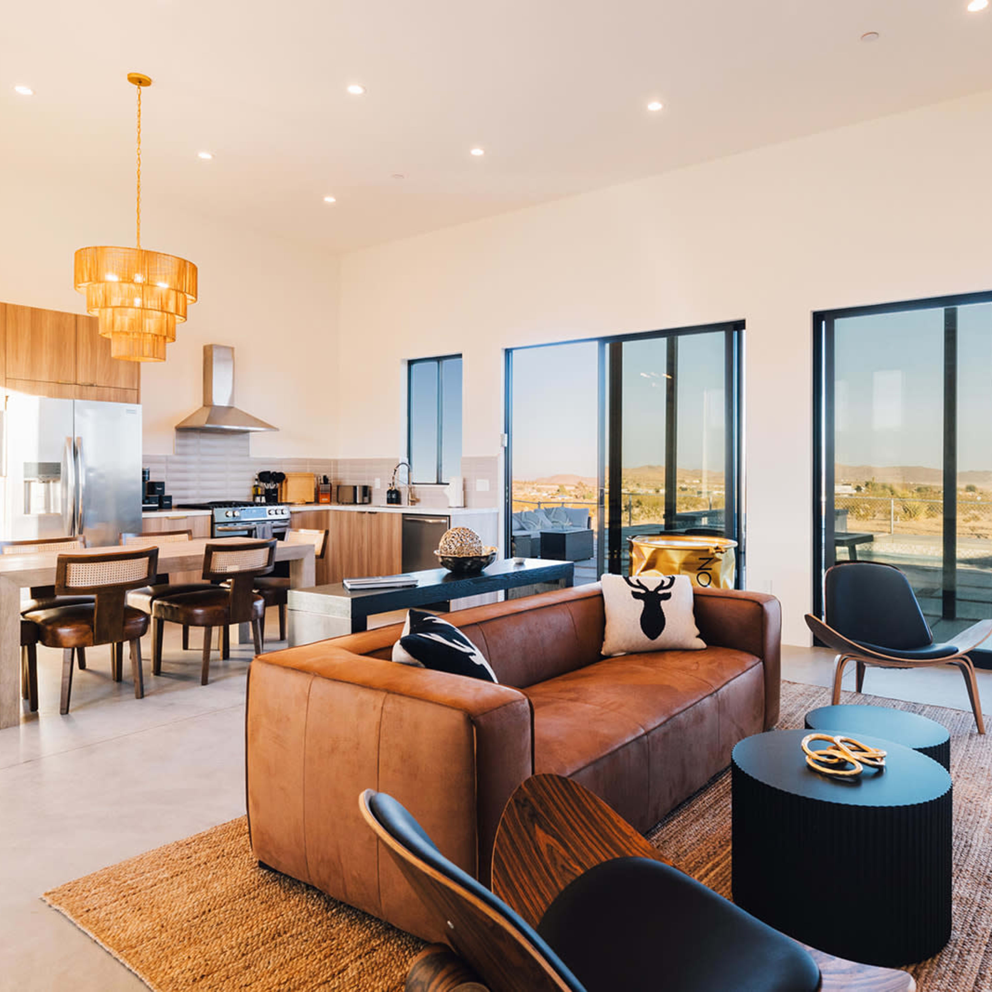 A modern open-concept living space featuring a kitchen, dining area, and living room with large windows offering a view of the outdoors.