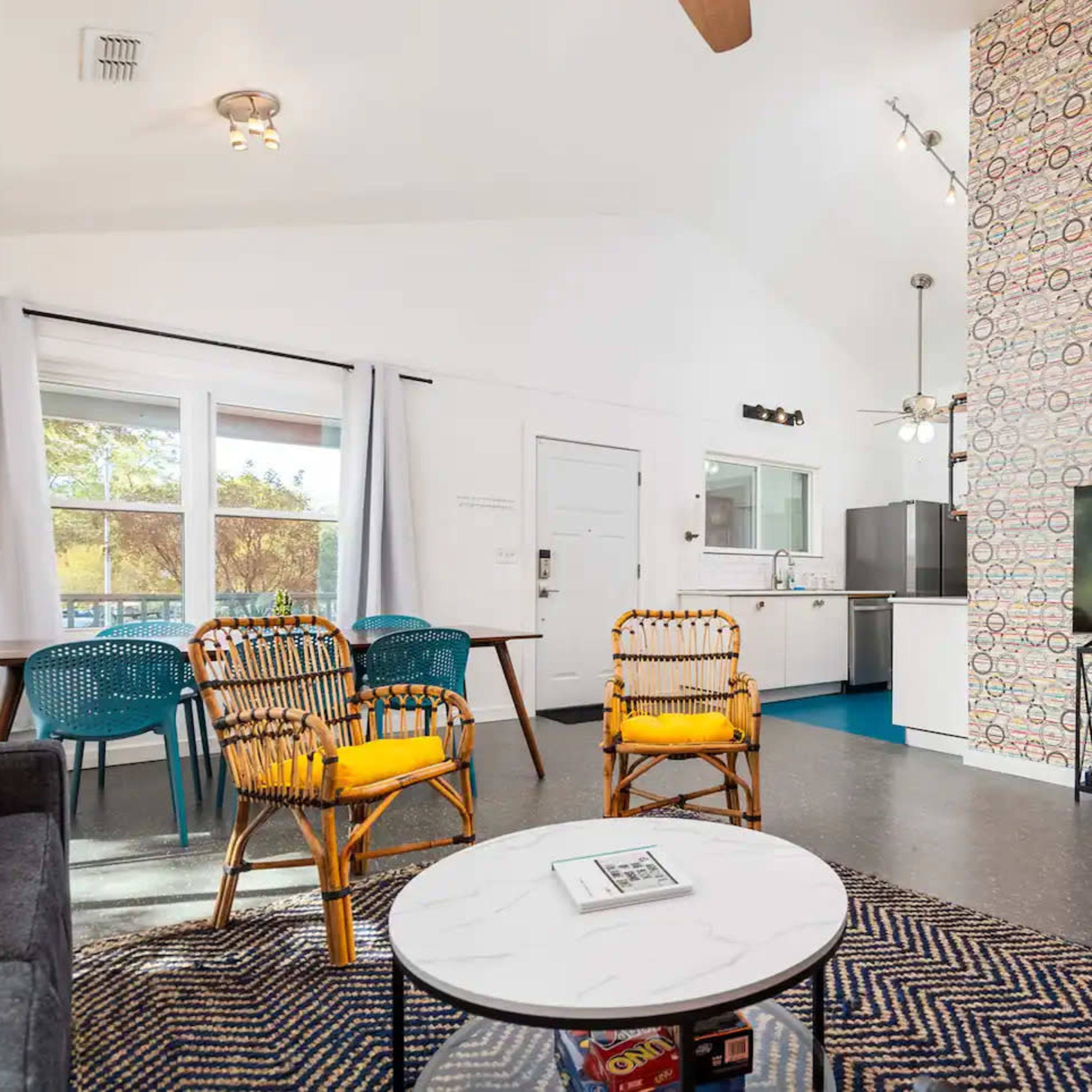 The living area features comfortable seating, a television, and a kitchen visible in the background with colorful decor on one wall.