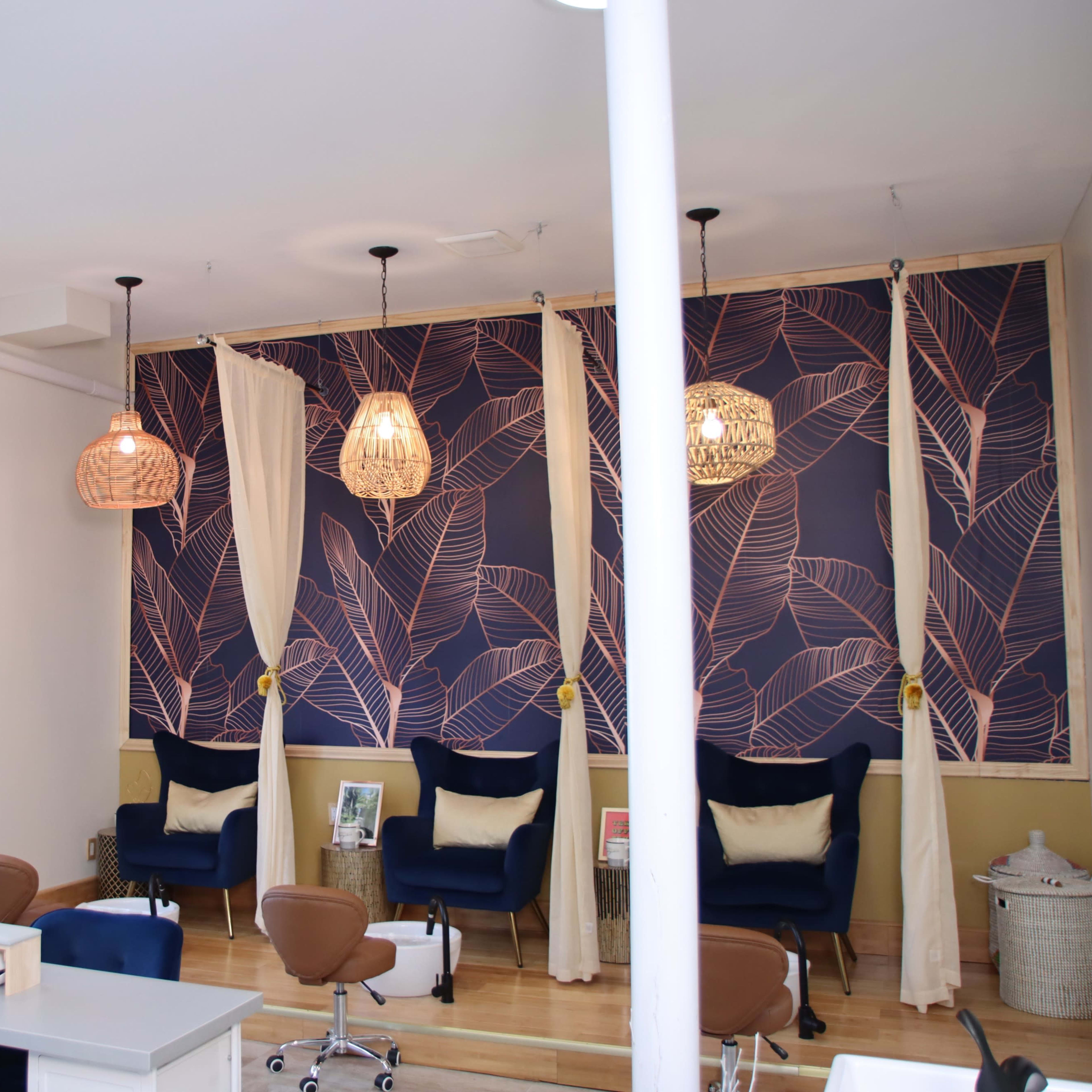A bright salon interior featuring stylish chairs, a wall with a leaf-patterned design, and hanging light fixtures.