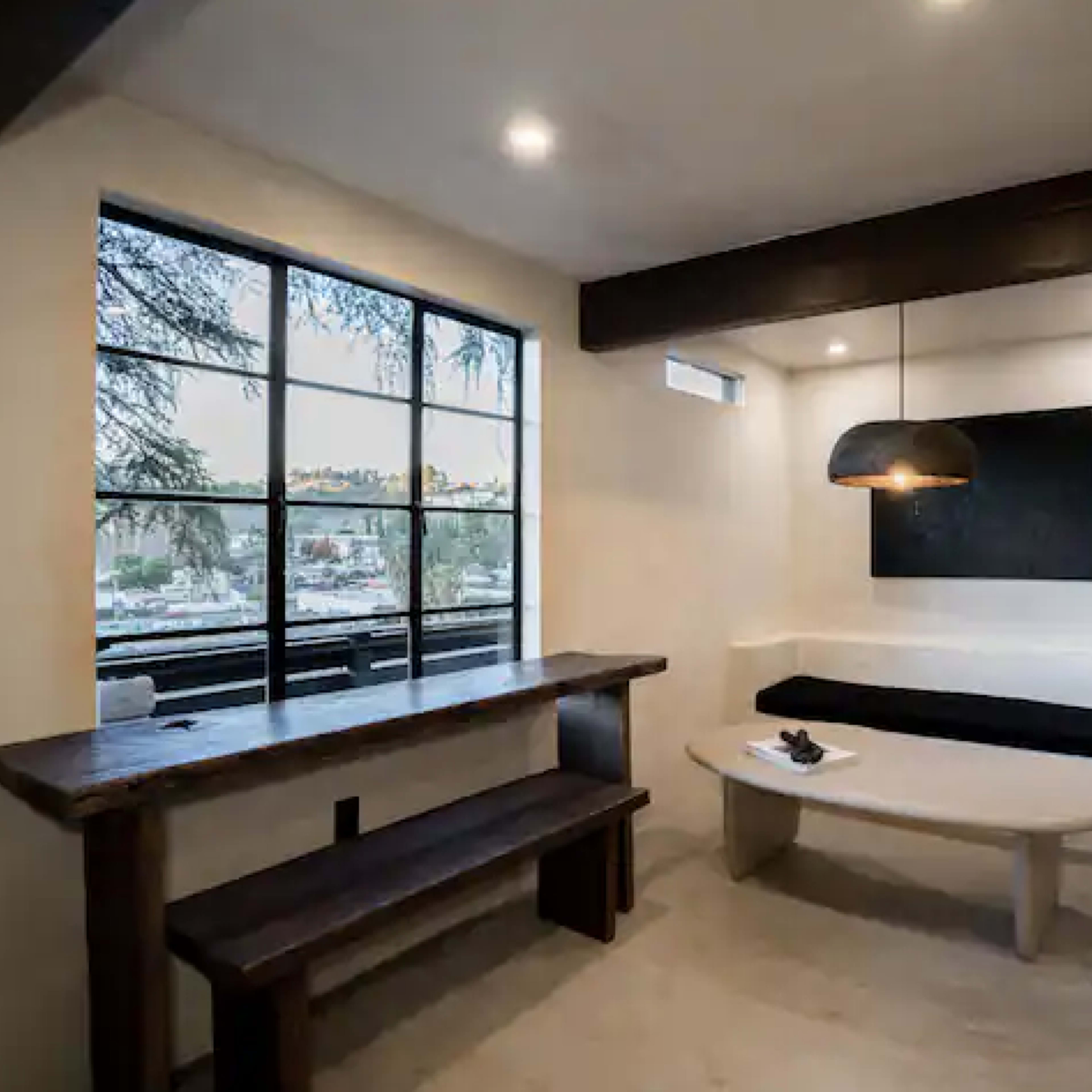 A modern, minimalistic living space with a bench, a round coffee table, and a large window offering a view of the outside.